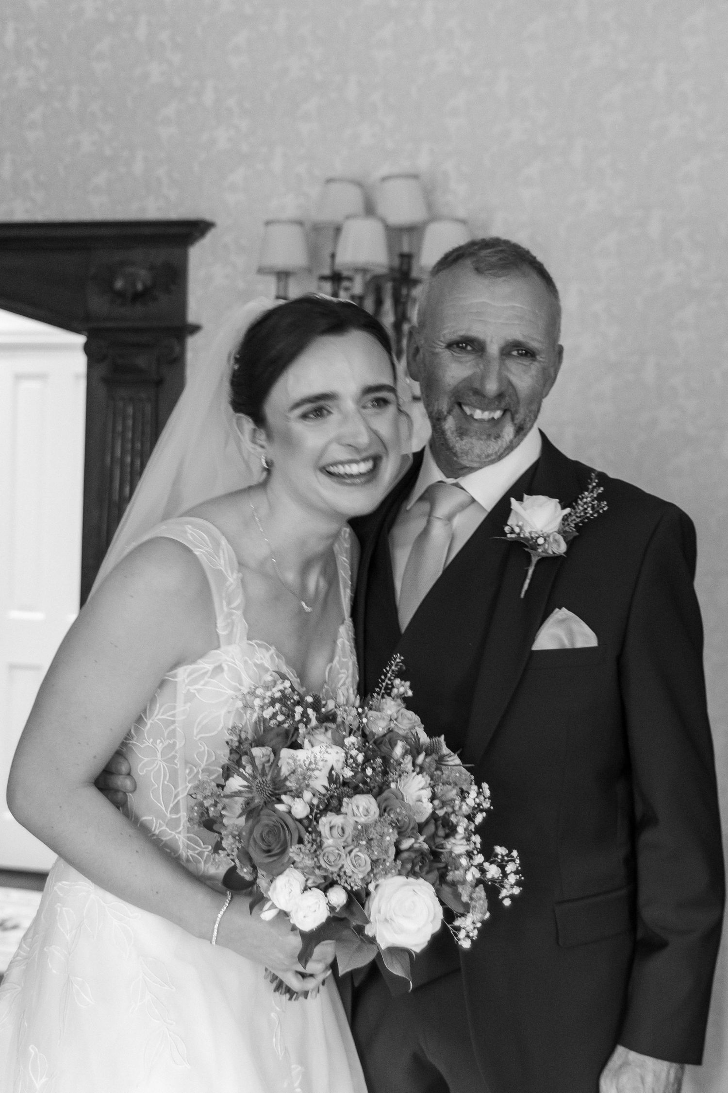 Black and white photo of a smiling bride holding a bouquet beside a man in a suit with boutonniere at a wedding.