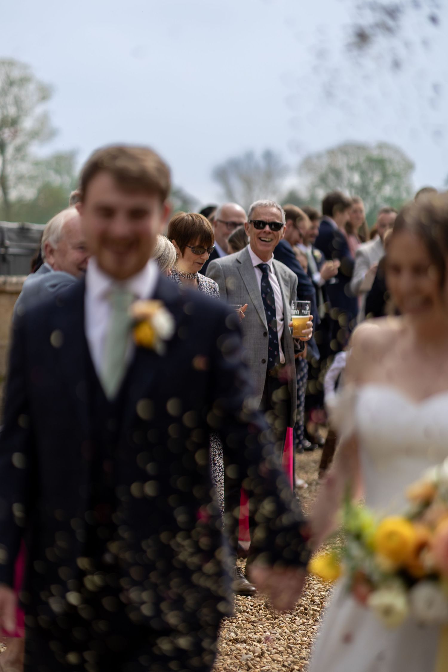 Wedding guests gathered outdoors for celebration with blurred foreground details.