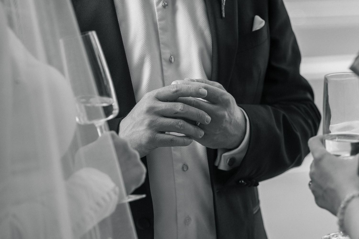 Black and white photo of groom placing wedding ring on bride's finger during ceremony.