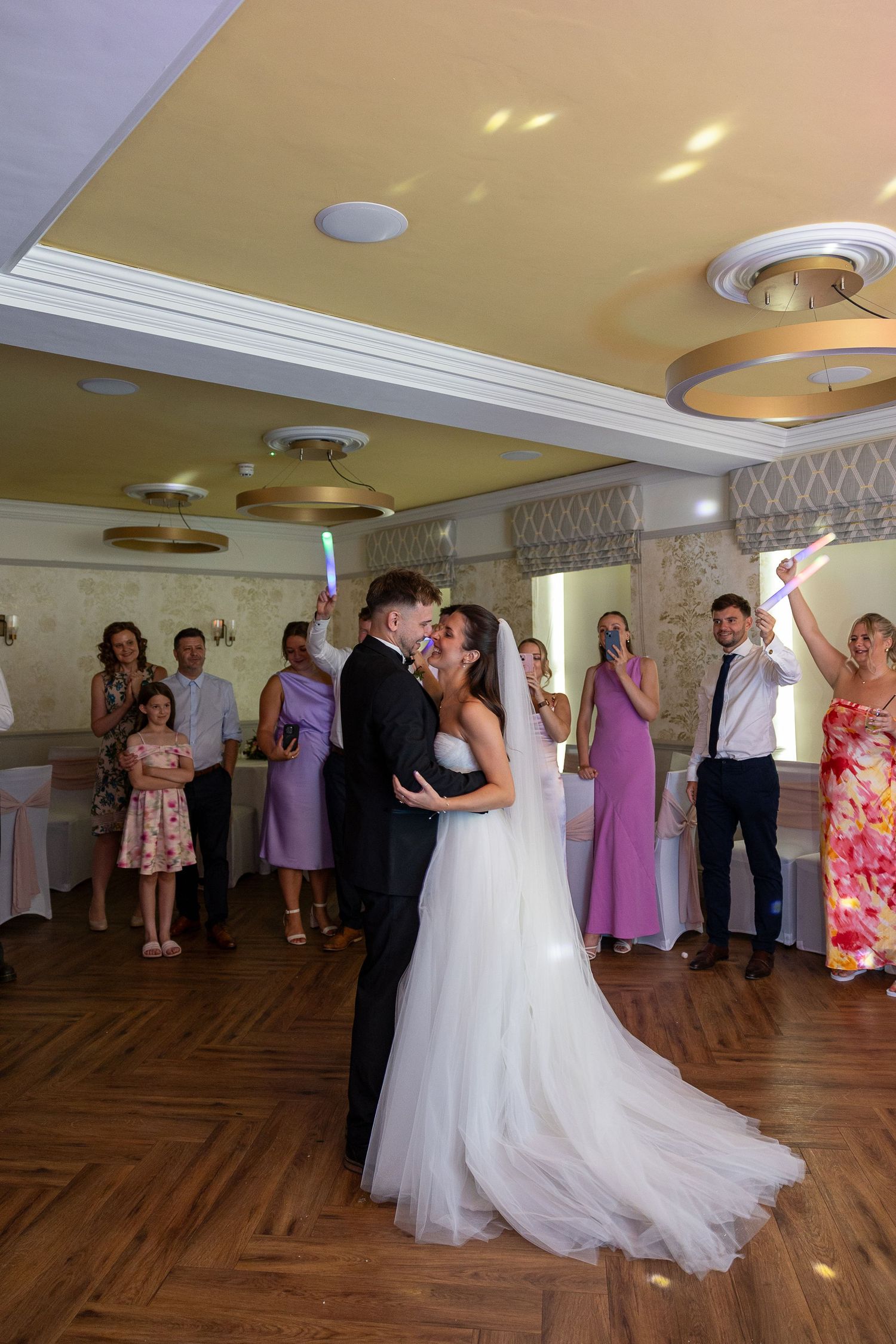 Wedding guests dance together on a wooden parquet floor during a reception celebration.