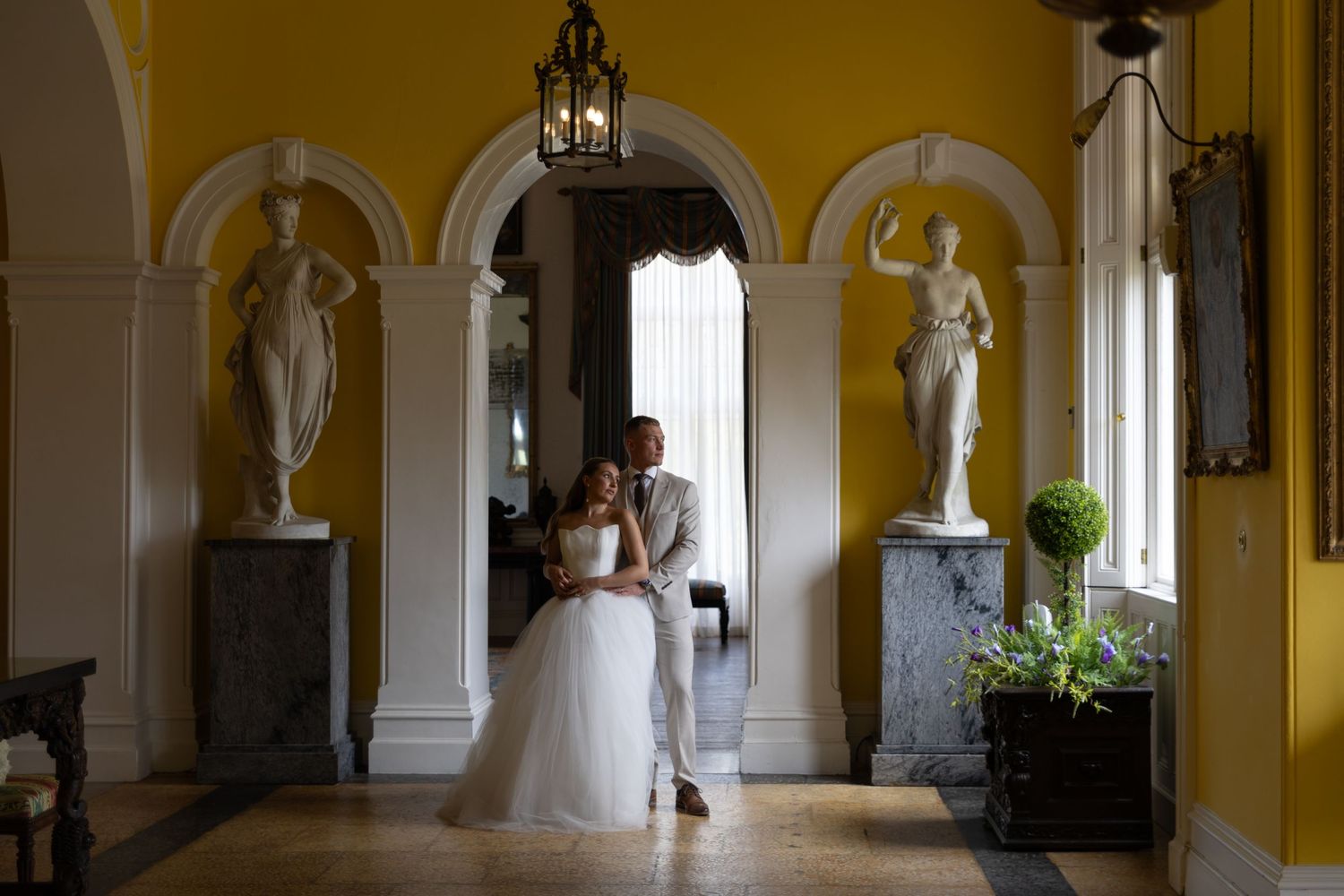 Elegant yellow-walled hallway with white columns and arched windows in a historic building.