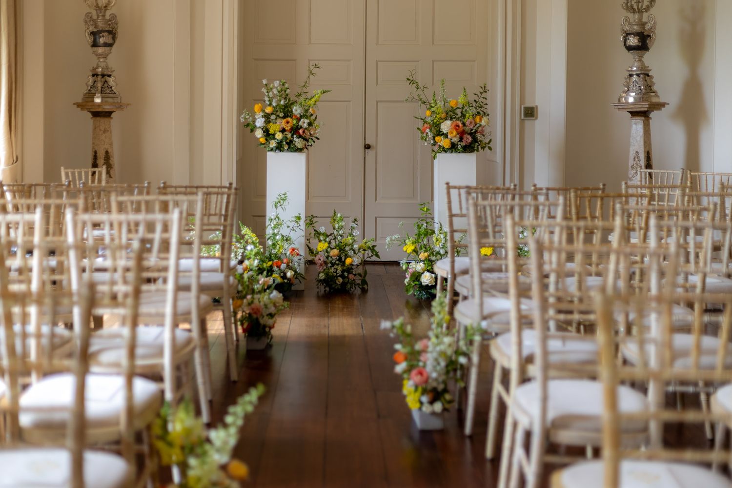 Elegant wedding venue setup with white chairs and floral decorations in natural light.