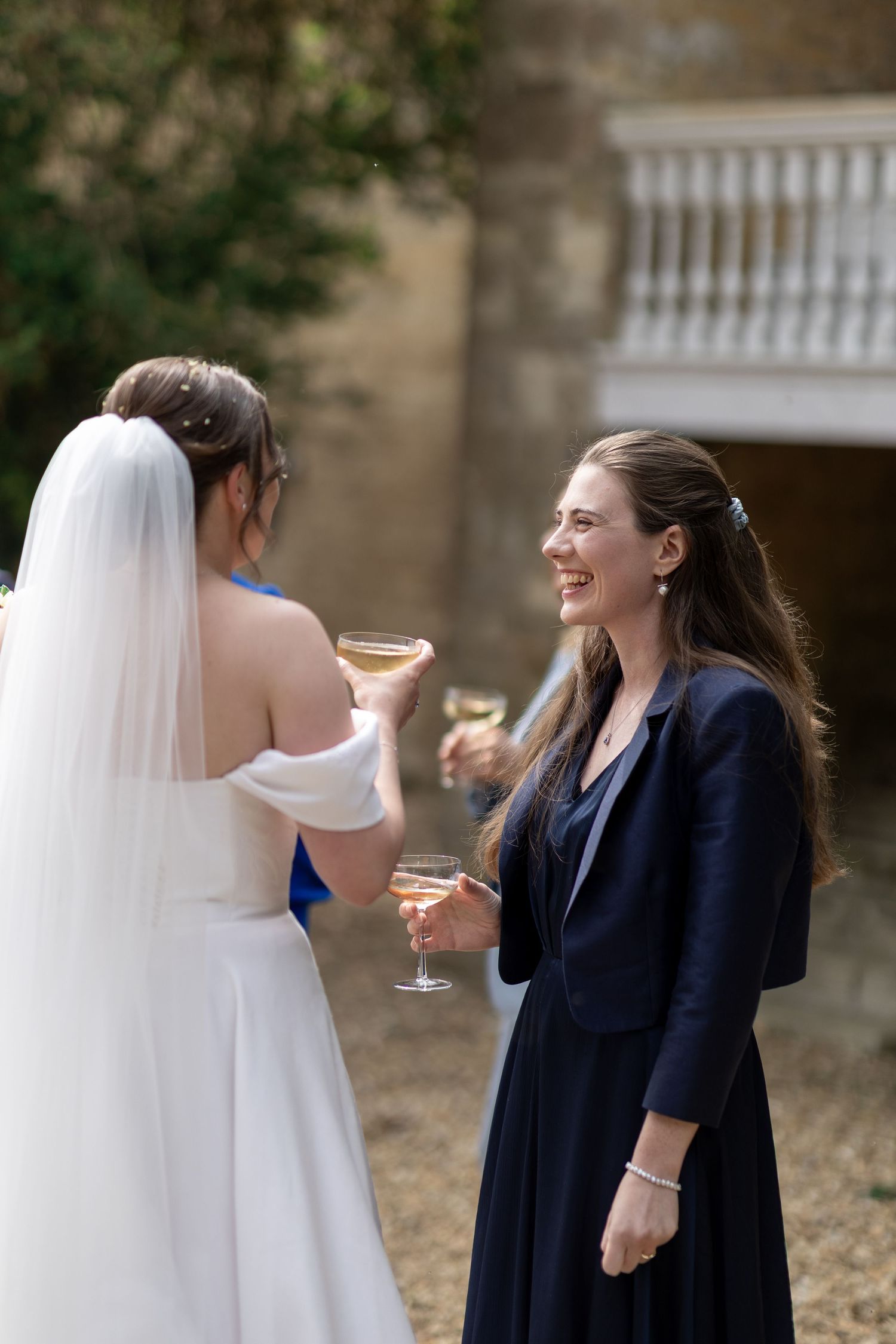 Two women share a joyful moment of laughter while standing outdoors at a formal event.