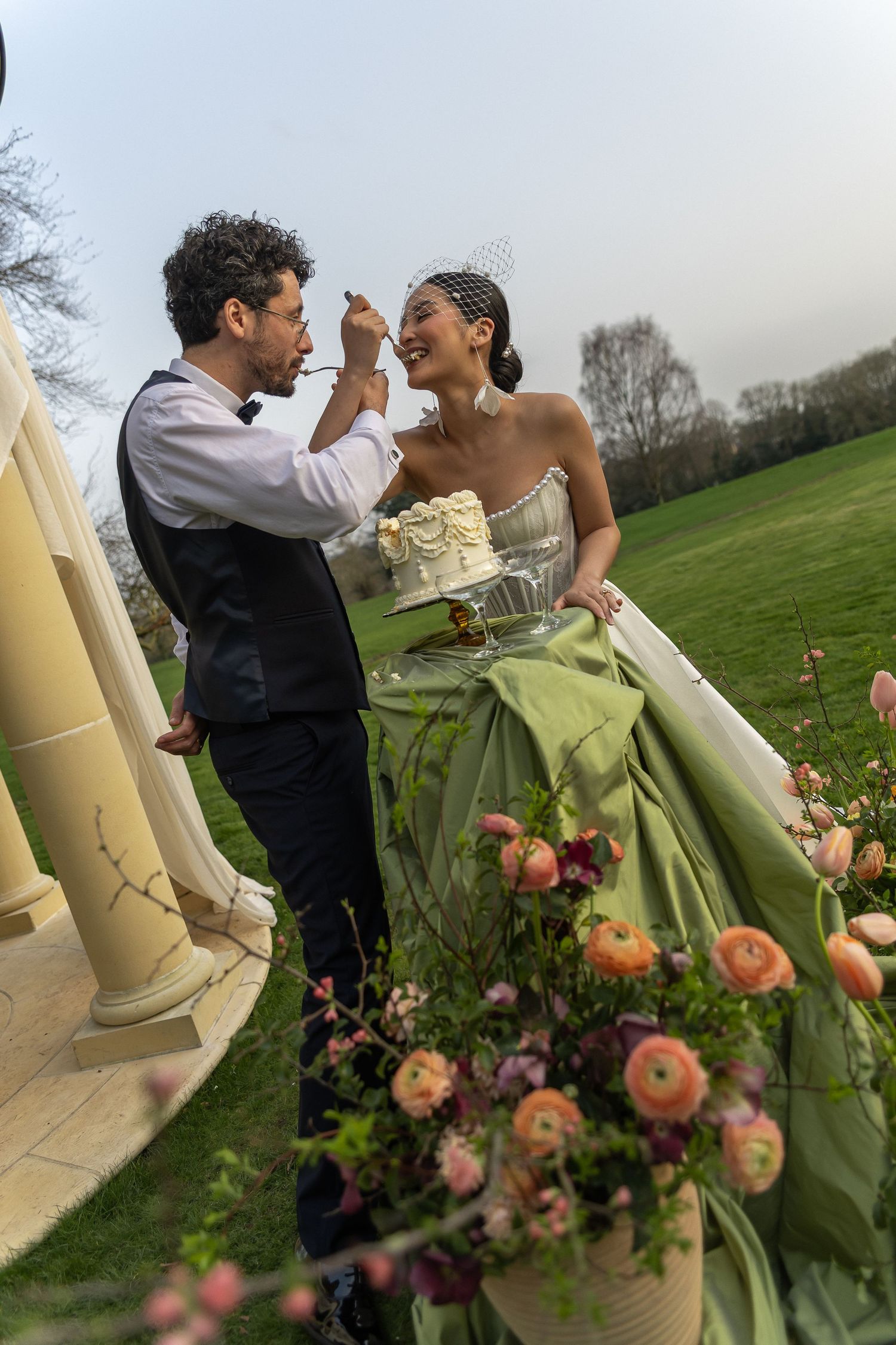 A romantic couple dancing outdoors near peach-colored roses and stone pillars at a wedding celebration.