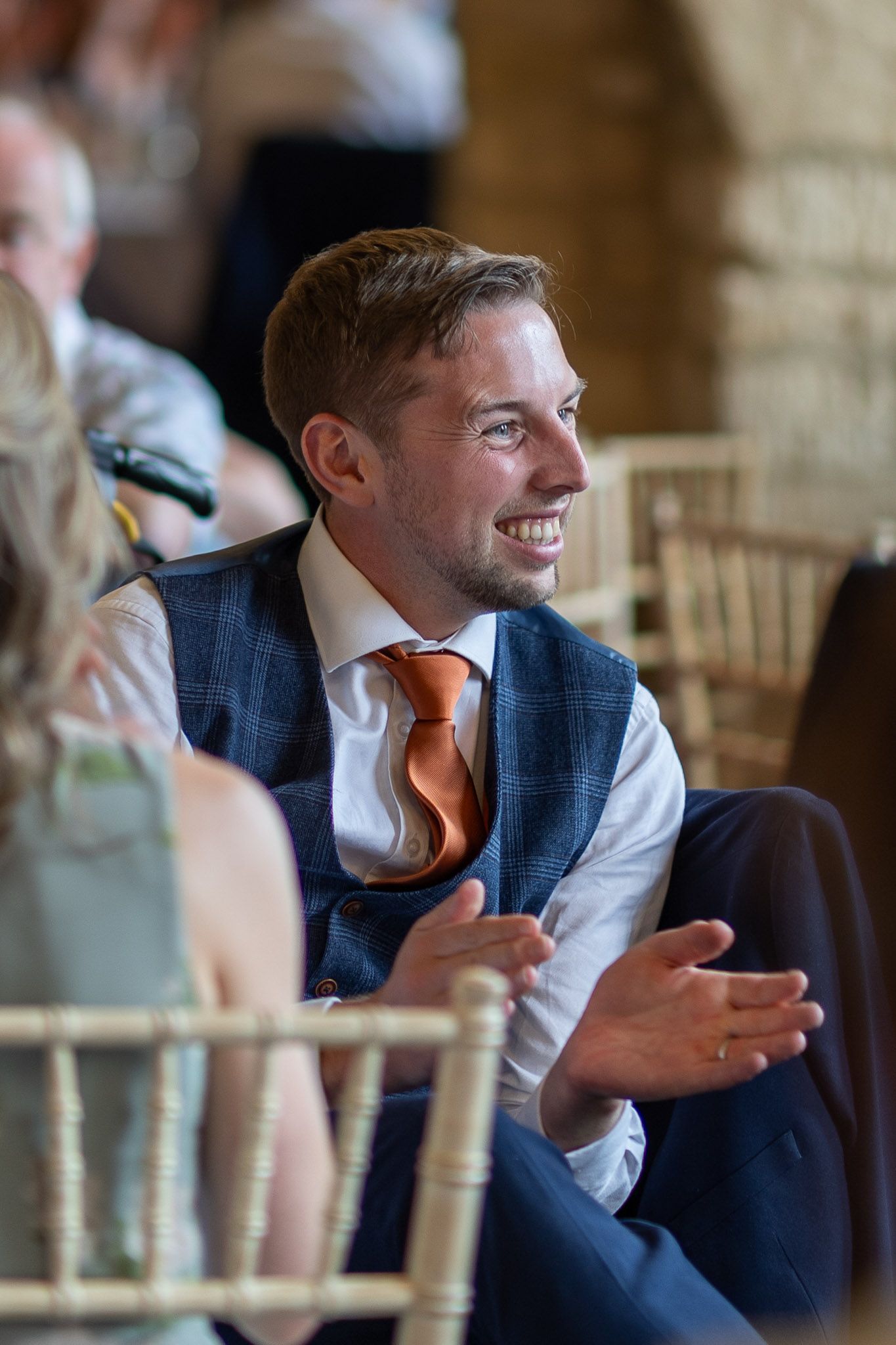 Wedding reception guest smiling during speeches in a rustic stone venue.