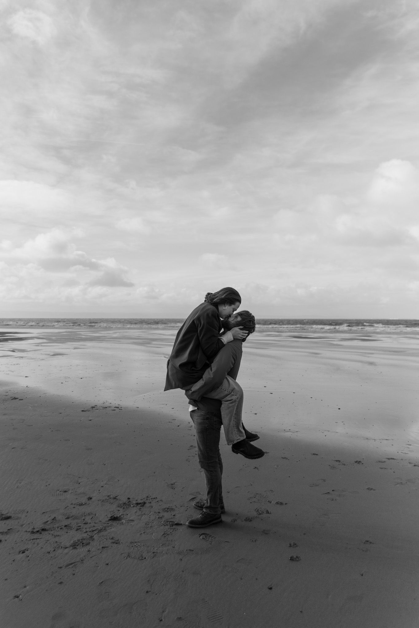 A couple sharing an intimate moment on a deserted beach in black and white.