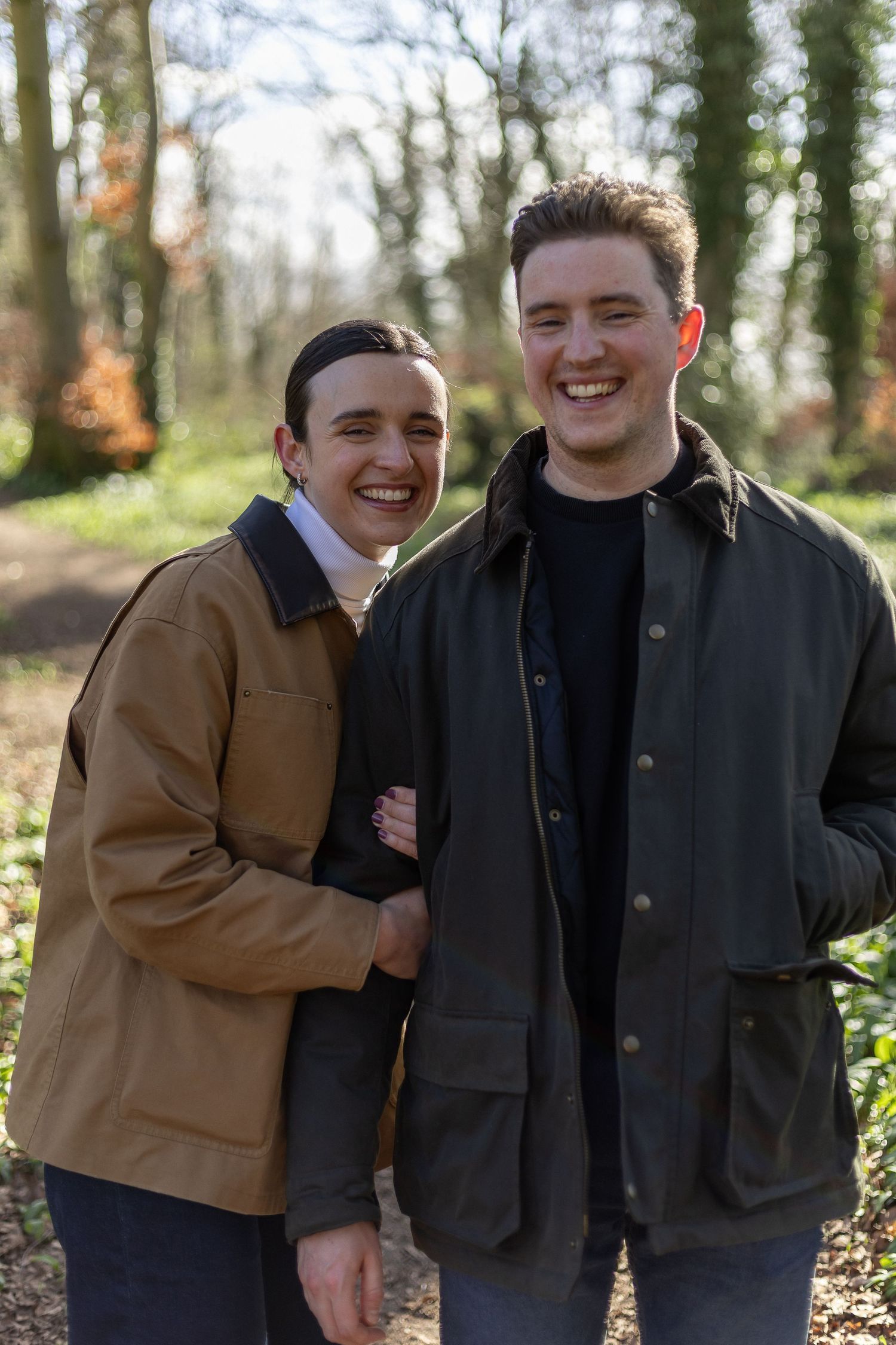 Two people share a joyful moment together while standing outdoors in a wooded area during autumn.