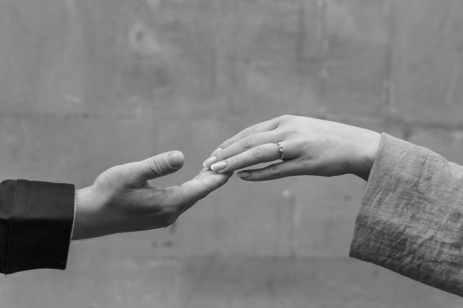 Black and white photo of two hands touching, with a diamond engagement ring visible on the womans finger.