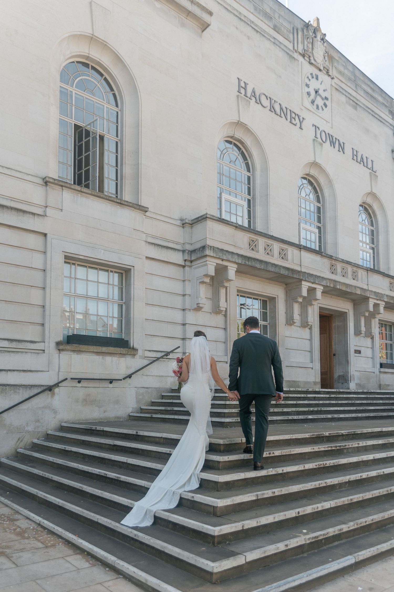Bride and groom walking up steps to Hackney Town Hall for their wedding ceremony in London.