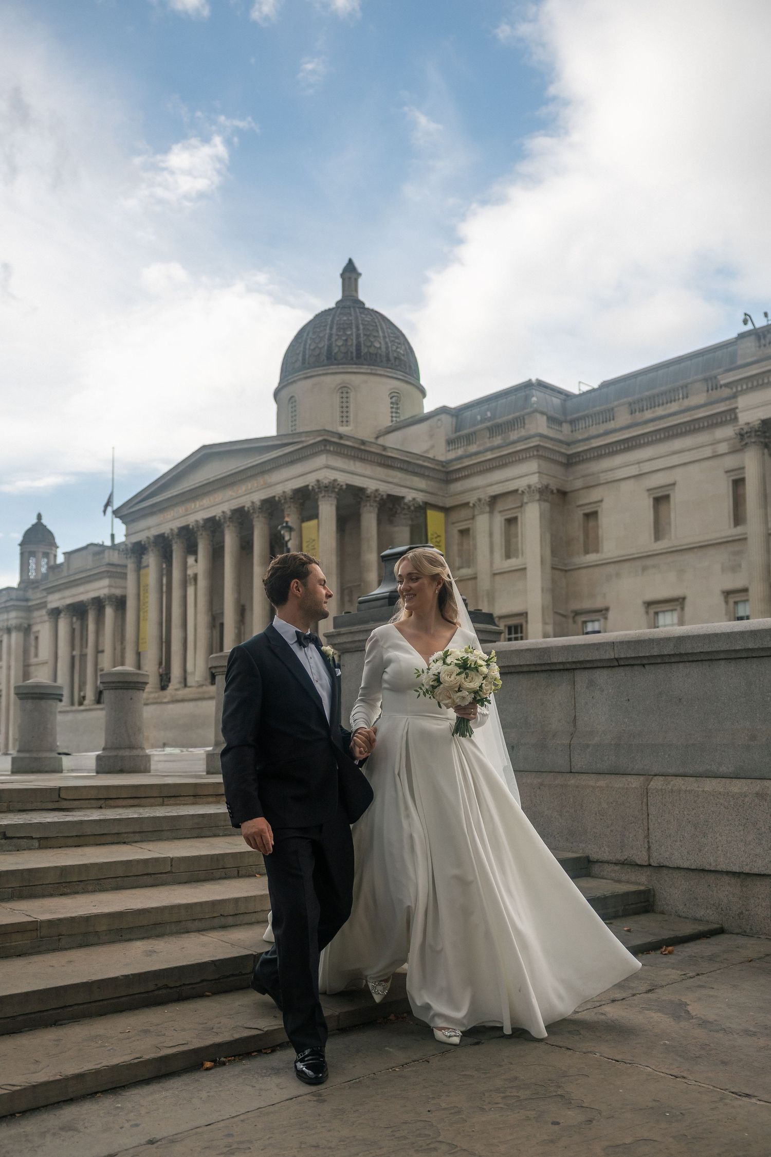 Bride and groom posing on steps outside the National Gallery in London on their wedding day.