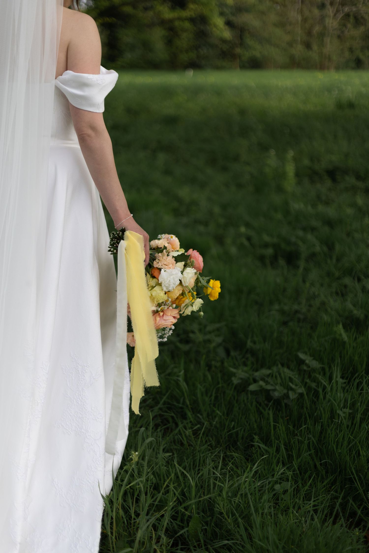 Person in white dress holding a colorful bouquet of flowers while standing in green grass field.