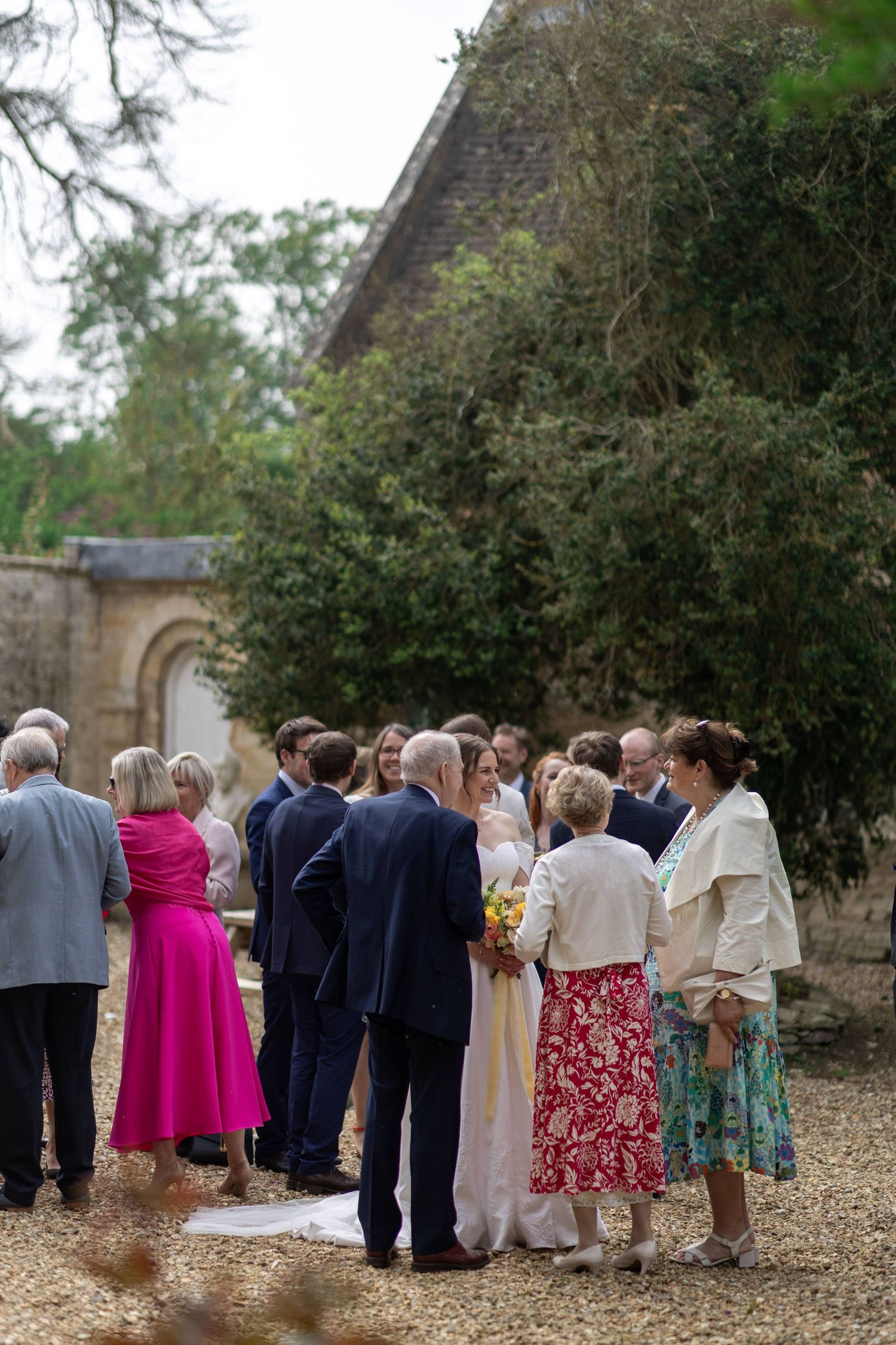 Wedding guests gathered outside a historic stone building on a gravel path.
