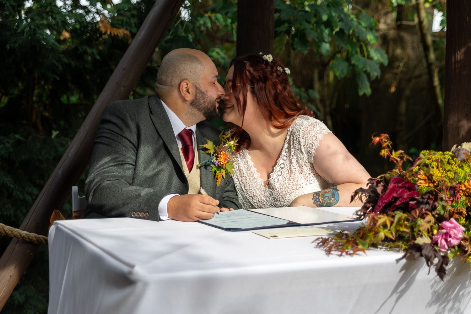 Couple shares an intimate moment on their wedding day surrounded by lush greenery and autumn flowers.