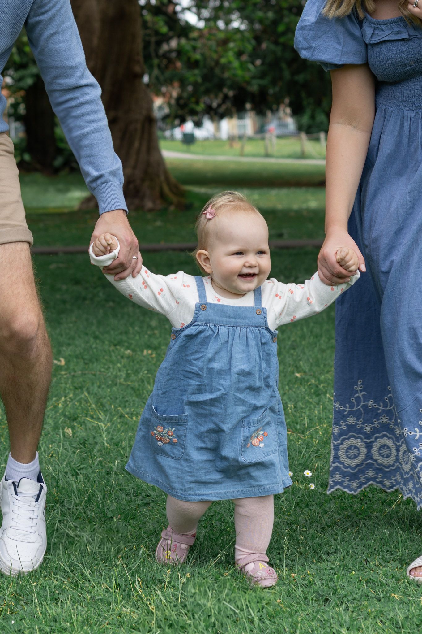 Close-up of tiny feet and legs walking on grass, with adults in blue clothing visible.