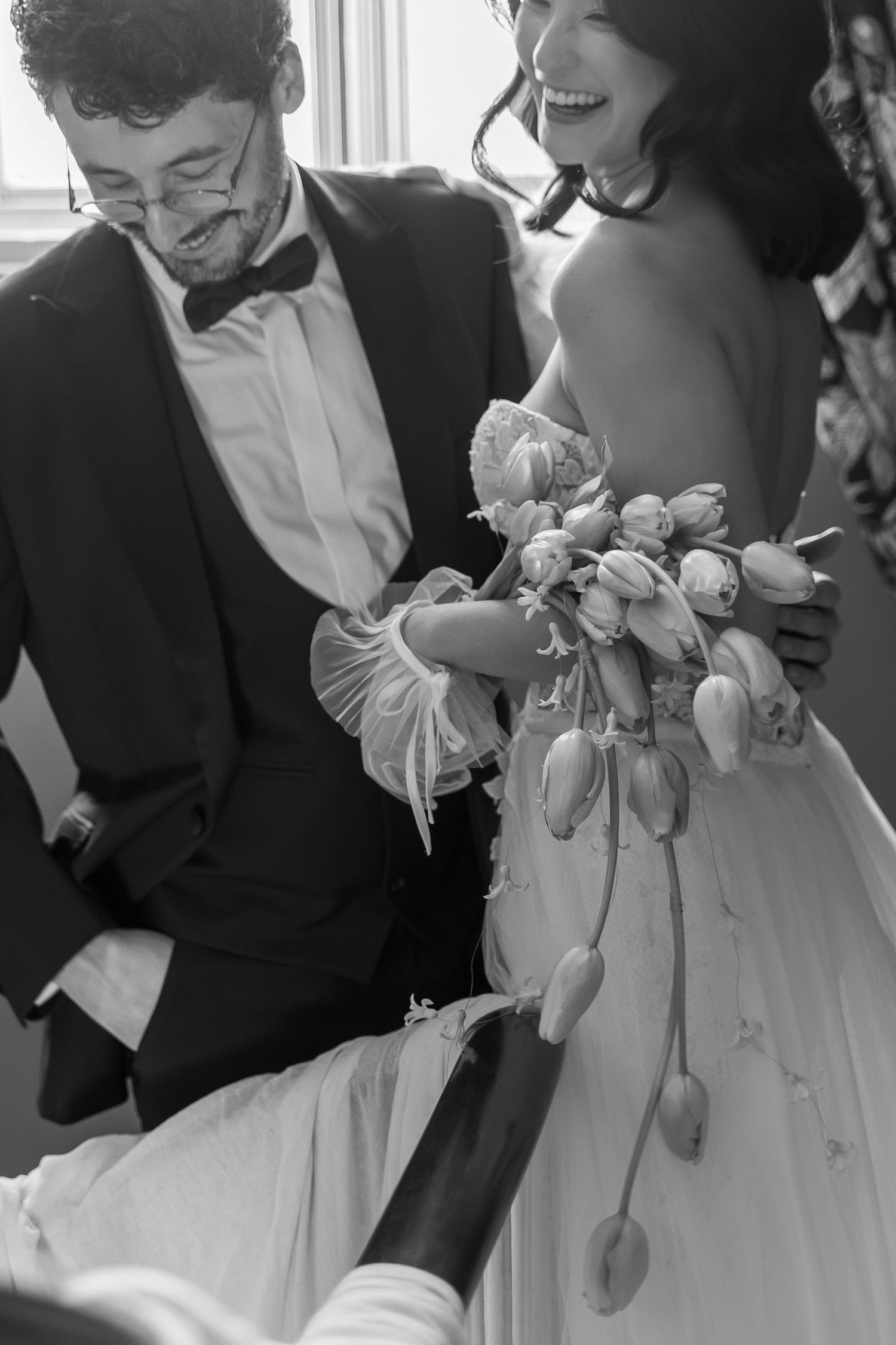 Black and white wedding photo showing couple laughing together while holding a floral bouquet.