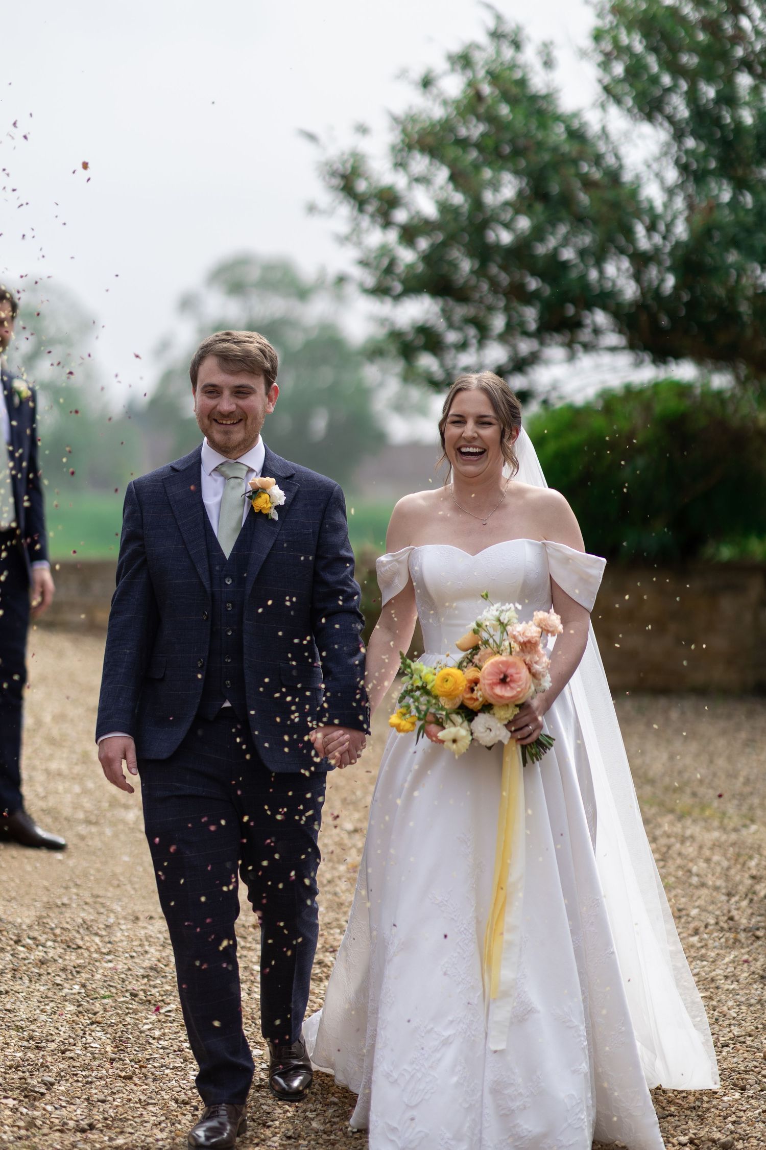 Wedding couple laughs joyfully while being showered with rice during an outdoor celebration.