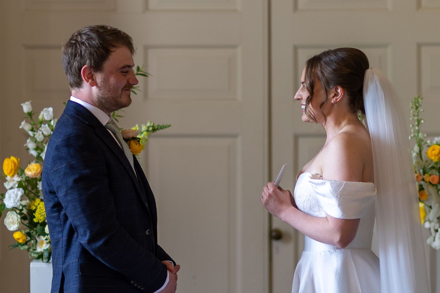 Bride and groom exchange vows at altar decorated with yellow and white floral arrangements during wedding ceremony.