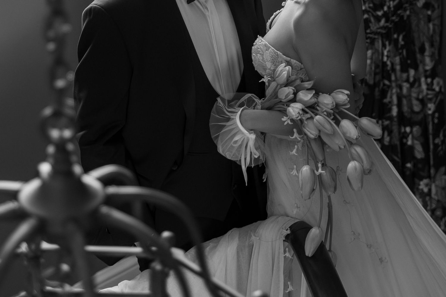 Black and white photo of a bride and groom embracing, bride holding a bouquet of tulips in an elegant wedding setting.