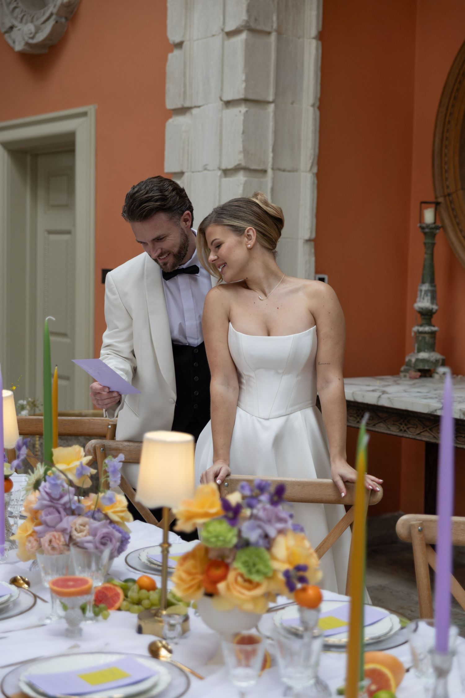 Romantic table setting with purple and orange flowers, candles, and intimate couple at dinner.