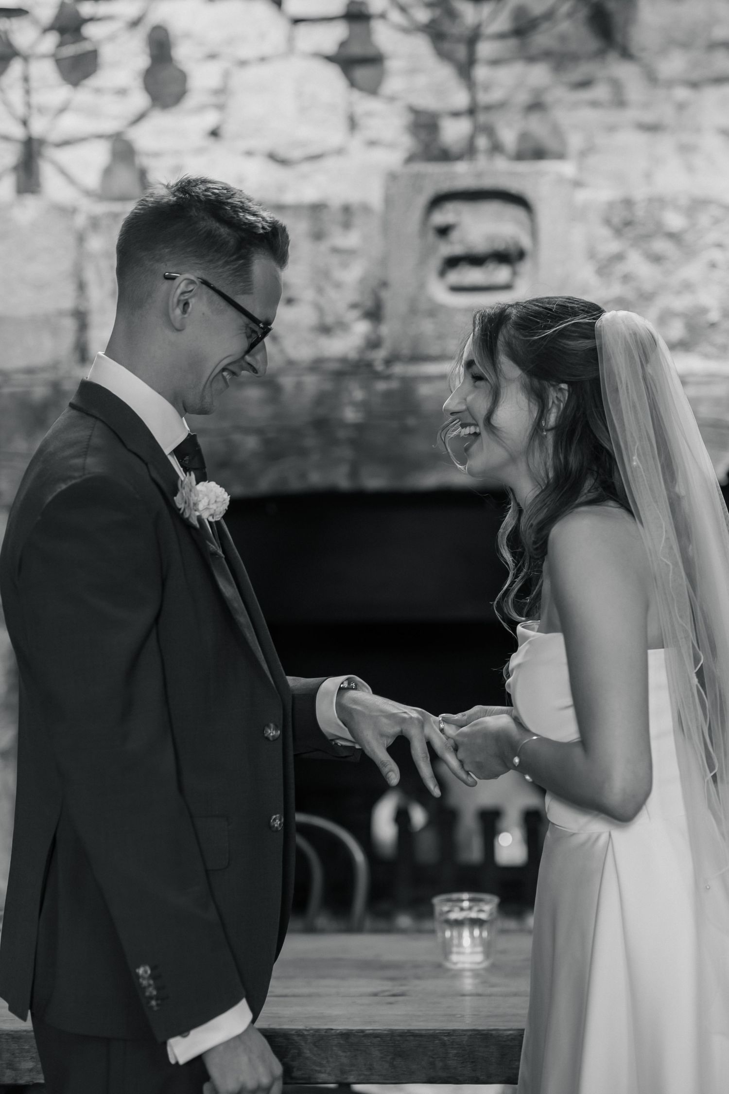 Black and white photo of a bride placing a wedding ring on the groom's finger during their ceremony.
