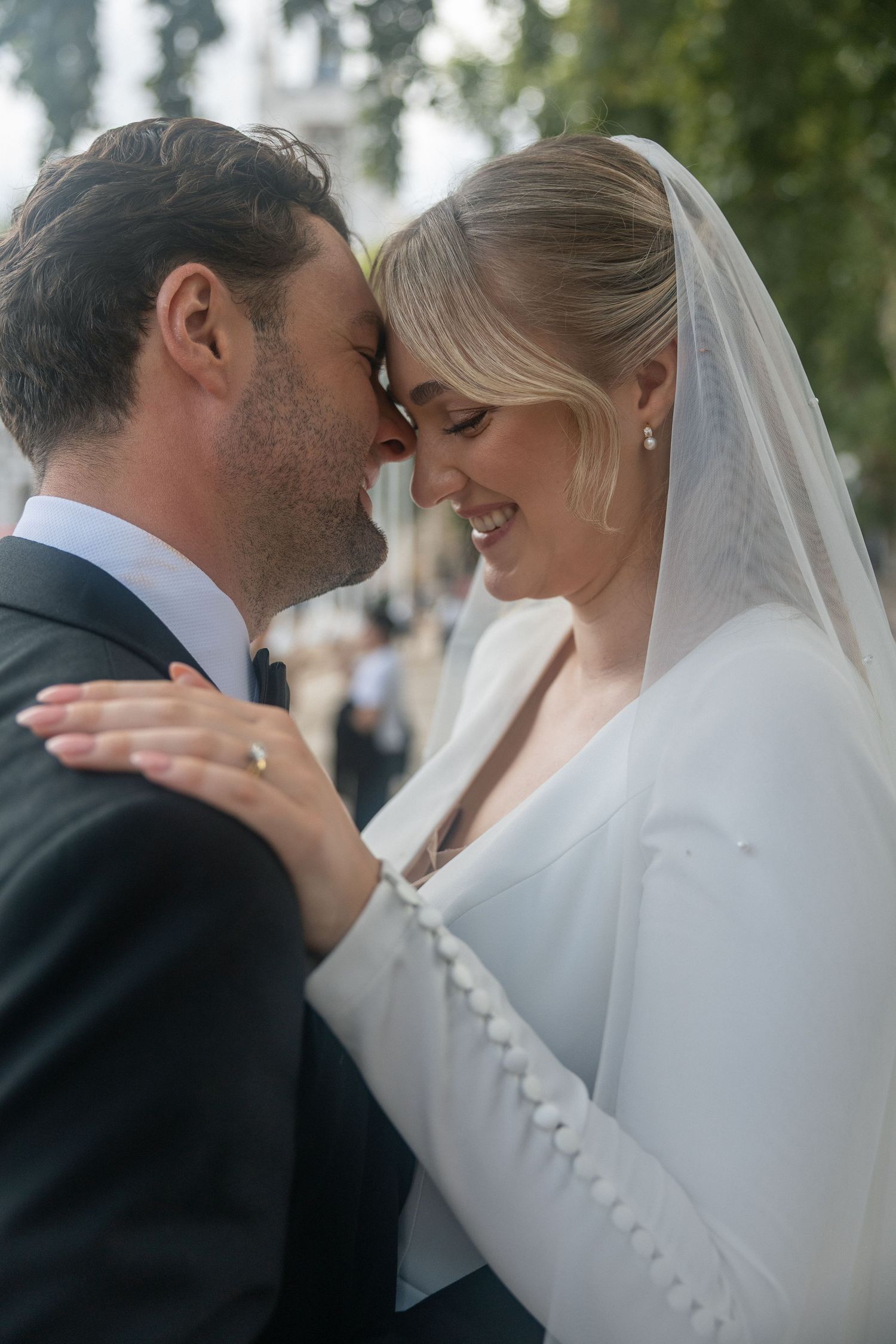 A bride and groom share an intimate moment, touching foreheads and smiling on their wedding day in London.