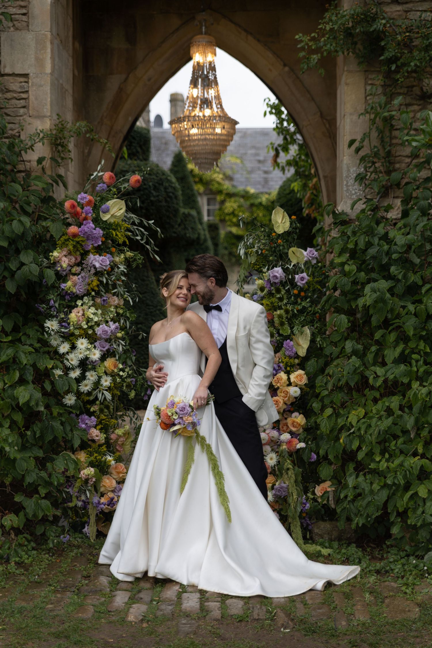 A couple shares a romantic moment in a lush garden setting with colorful floral arrangements.