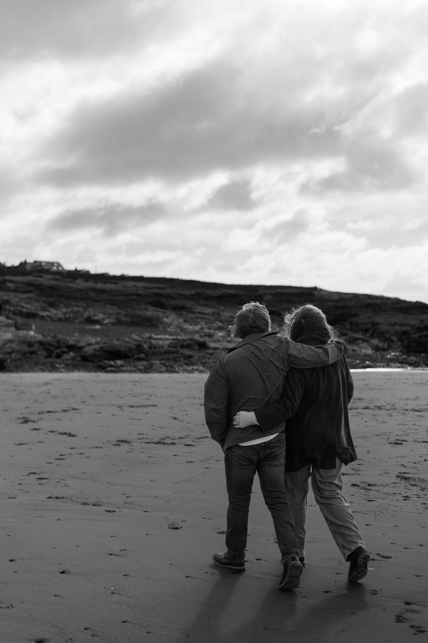 Black and white photo of friends walking together on a dramatic coastal landscape.