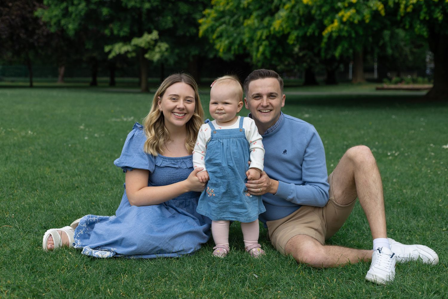 A family relaxes together on grass during an outdoor photo session in coordinating blue attire.