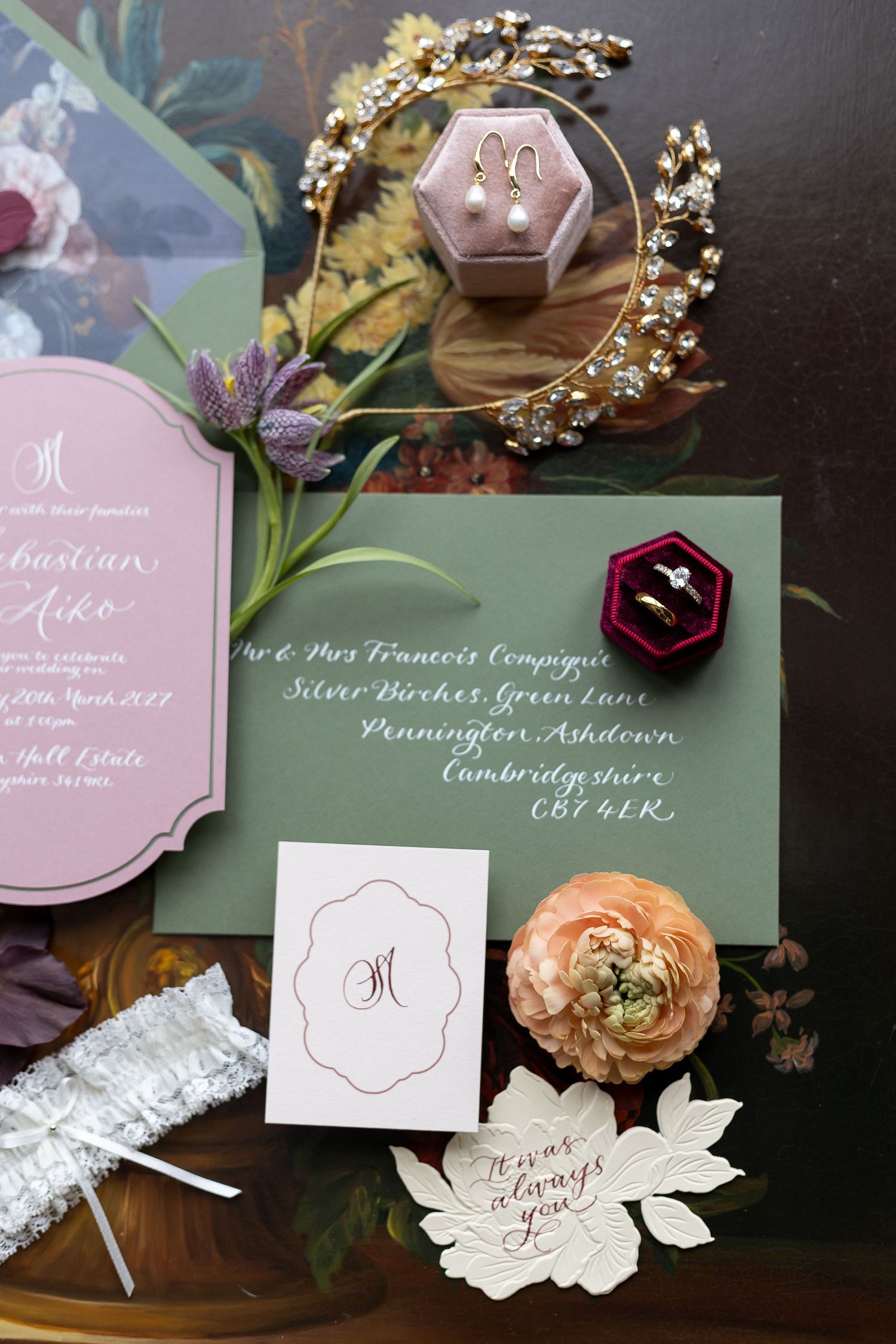 Wedding stationery suite featuring pink and white invitations with calligraphy alongside floral elements and jewelry.