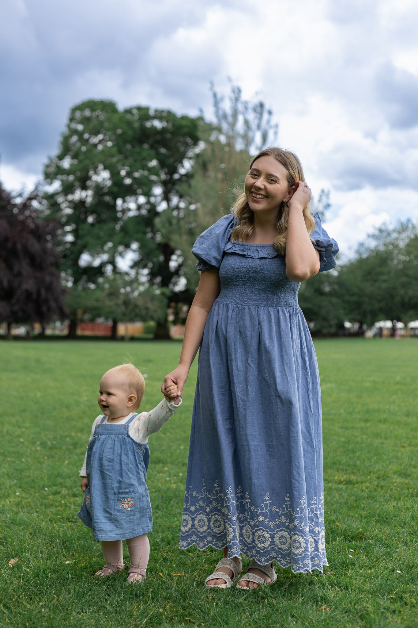 Mother and baby in coordinating blue outfits share playful moment on grassy field.