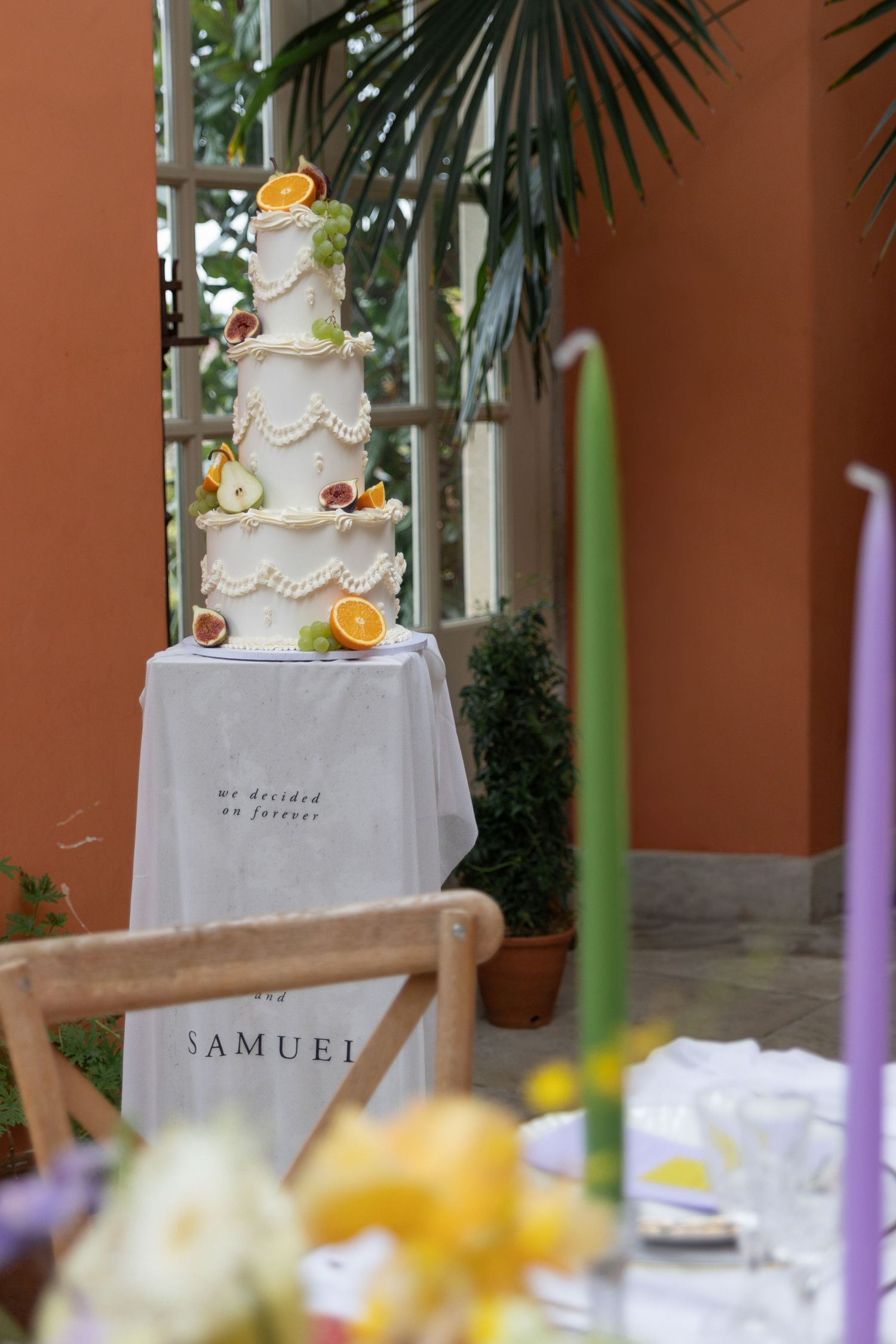 Elegant white wedding cake with orange citrus decorations displayed at a reception table with soft lighting and greenery.
