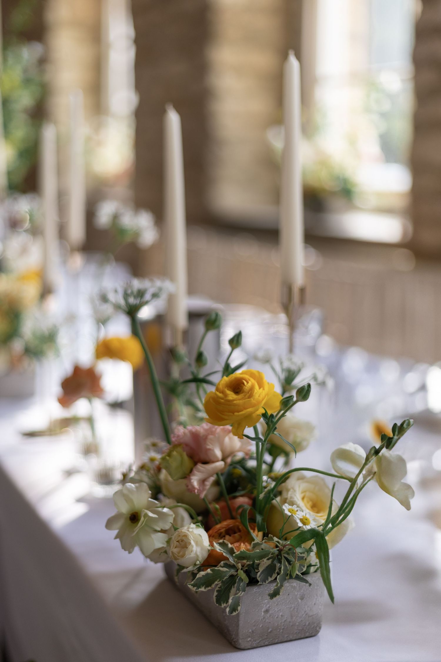 Elegant wedding table centerpieces featuring yellow ranunculus and white flowers in concrete planters.