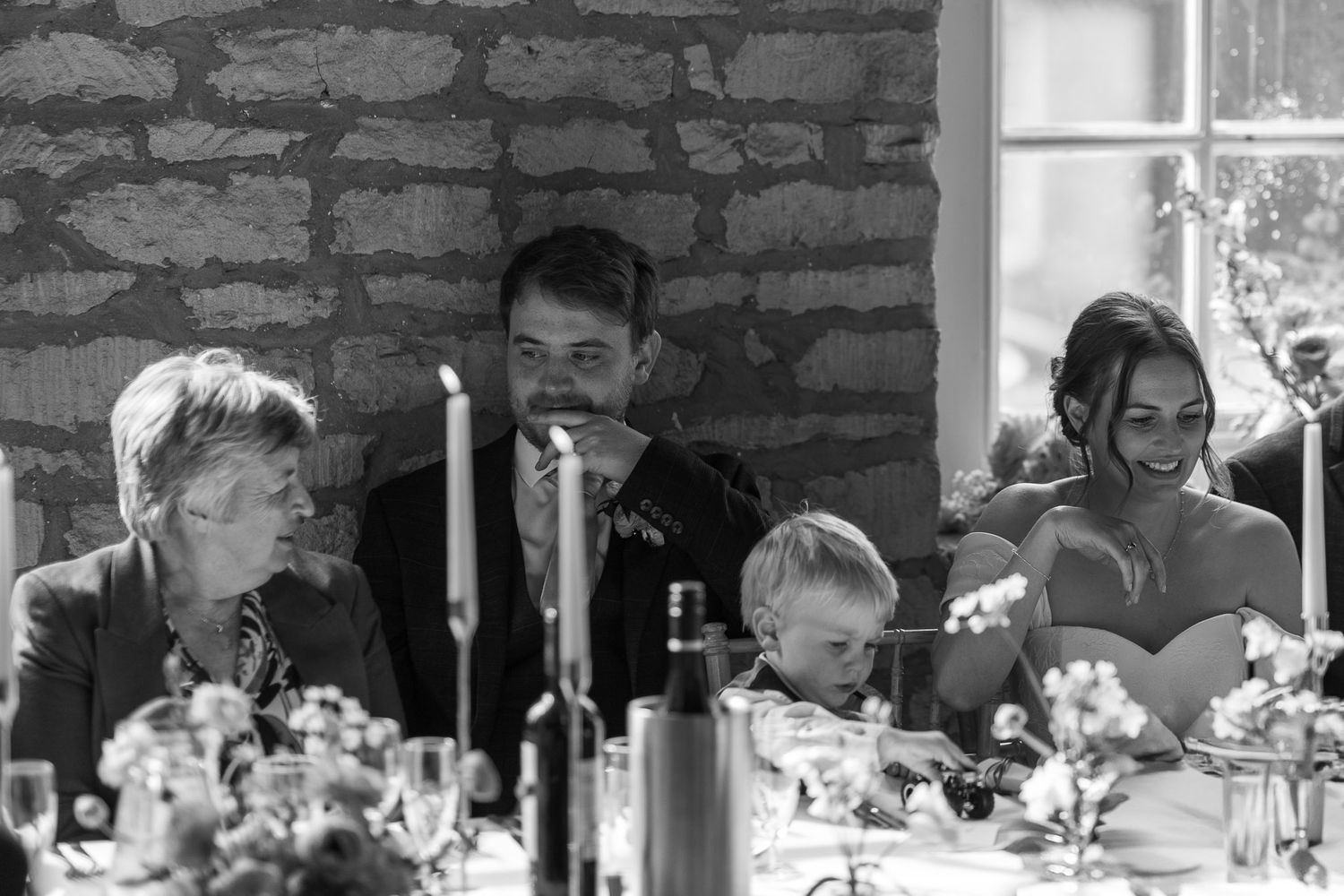 Wedding guests seated at long tables in a rustic stone venue with natural lighting.