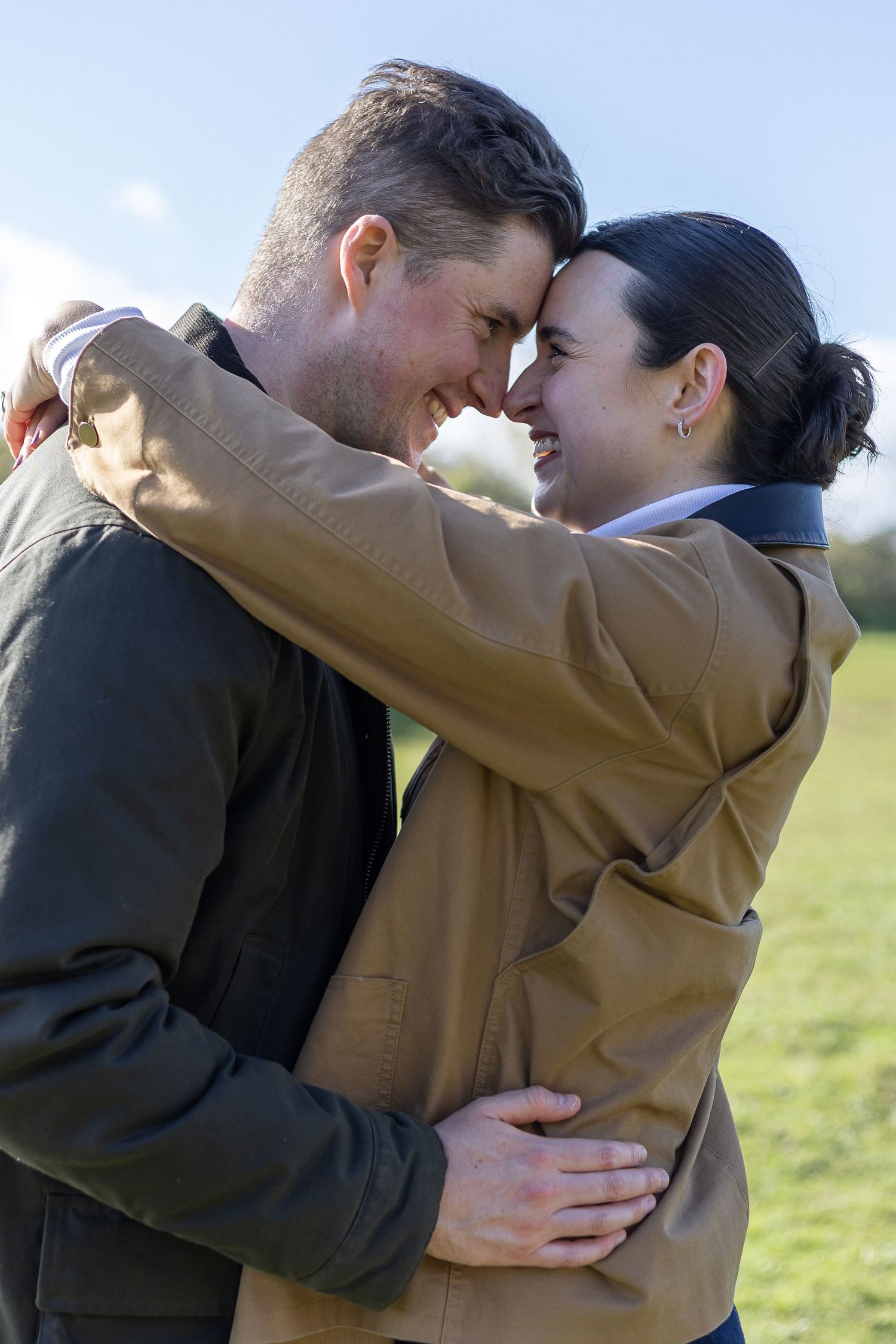 Two people share an intimate moment while embracing outdoors against a scenic countryside backdrop.