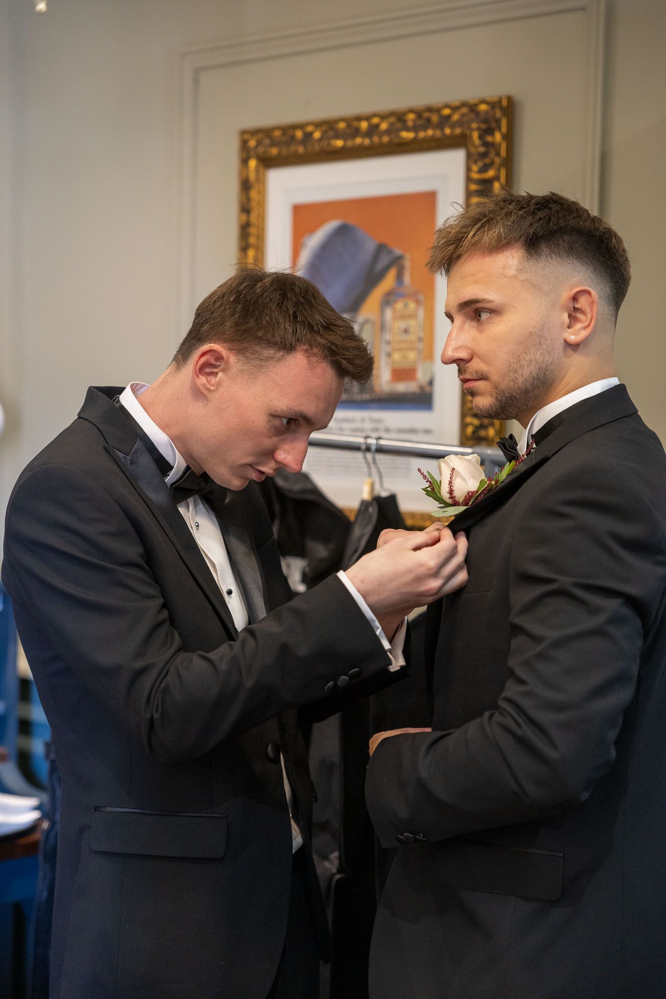 Men in formal attire help each other with bow ties and finishing touches before an event.