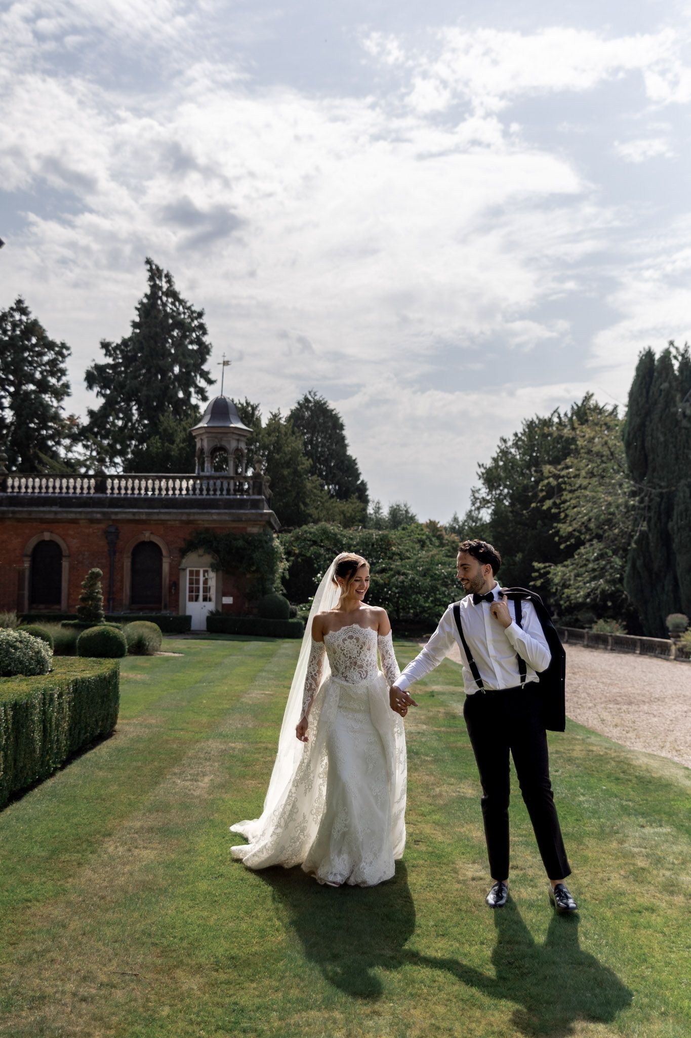 A wedding couple walking on manicured grounds of a historic estate with brick architecture.