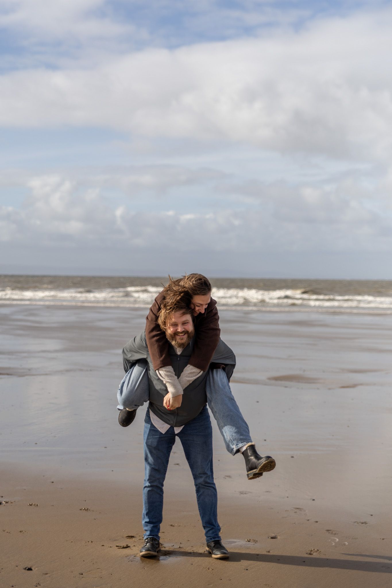 Two people share a playful dance move on a cloudy beach with waves crashing in the background.