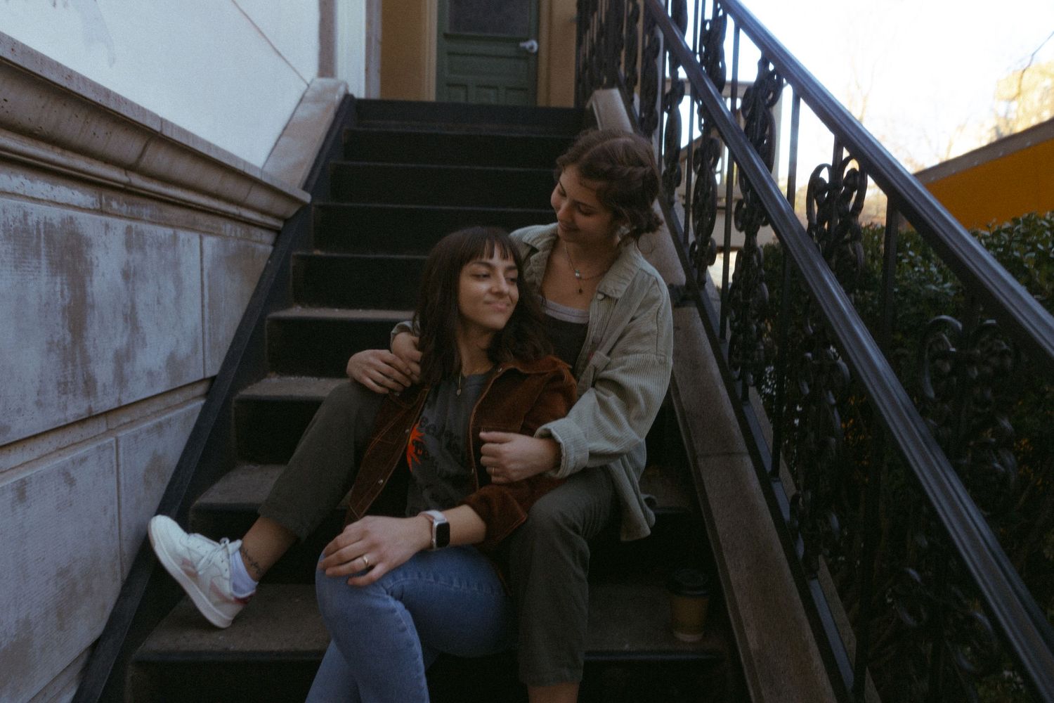 Couple sitting on outdoor staircase steps together holding a small dog in urban setting.