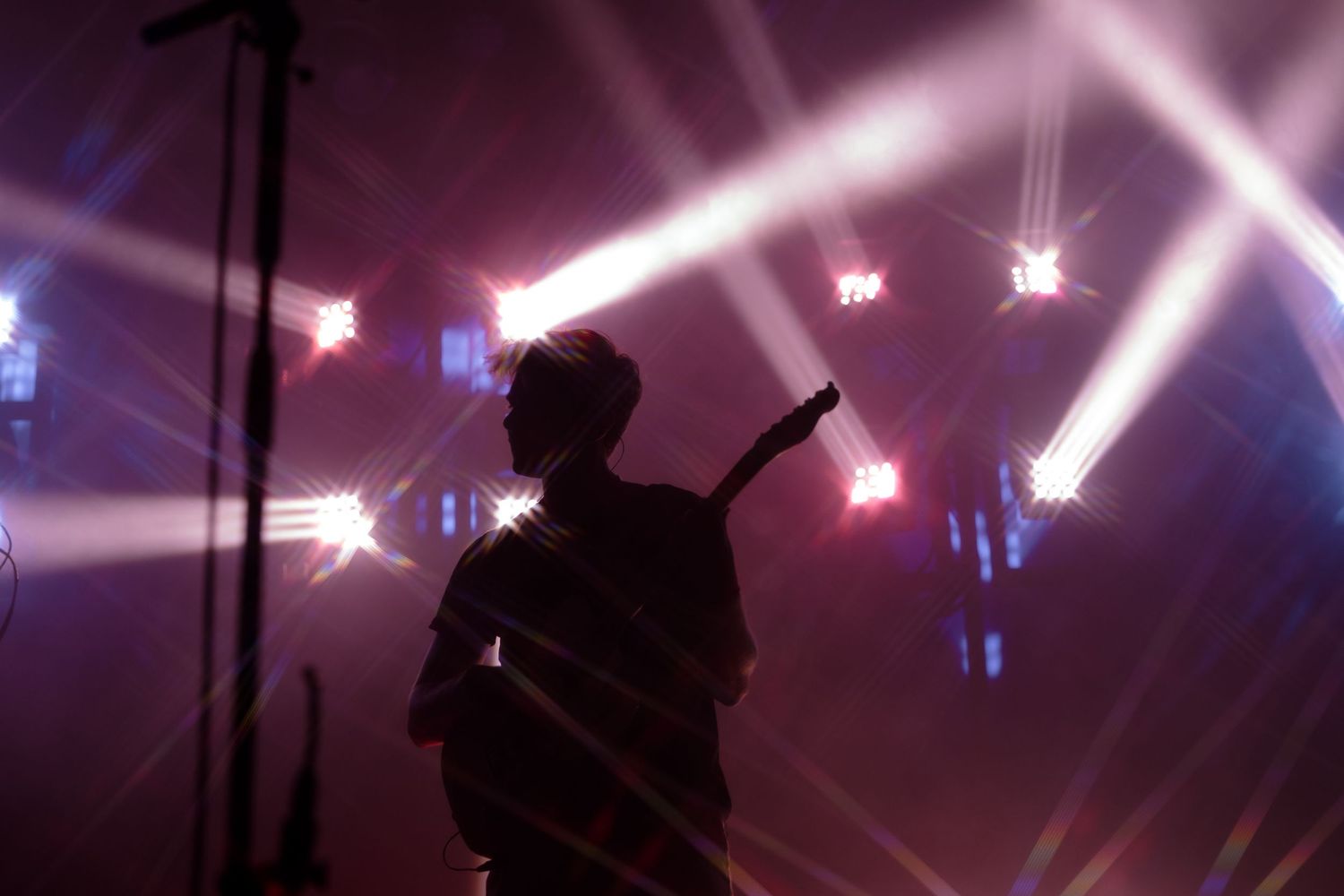 Silhouette of a guitarist performing on stage surrounded by dramatic star-burst concert lighting effects.