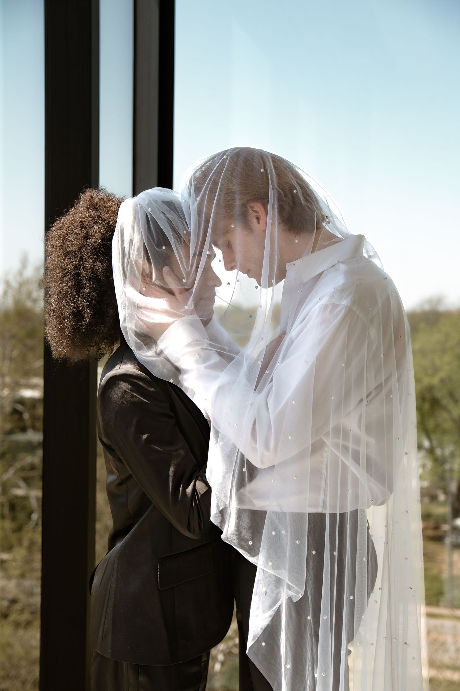 Two brides share an intimate moment under a white veil during their wedding ceremony.