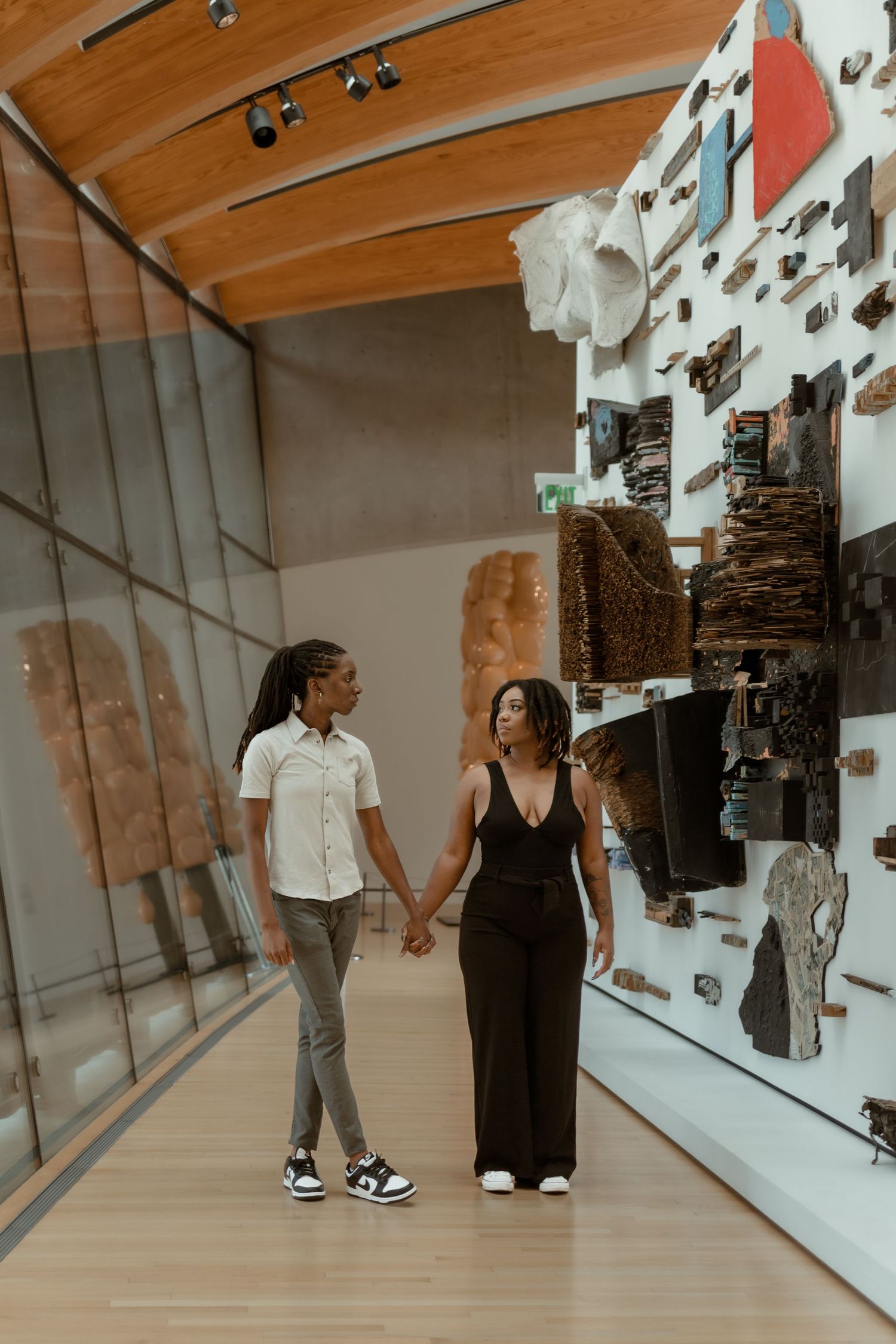 Two women hold hands while walking through a modern art museum gallery.