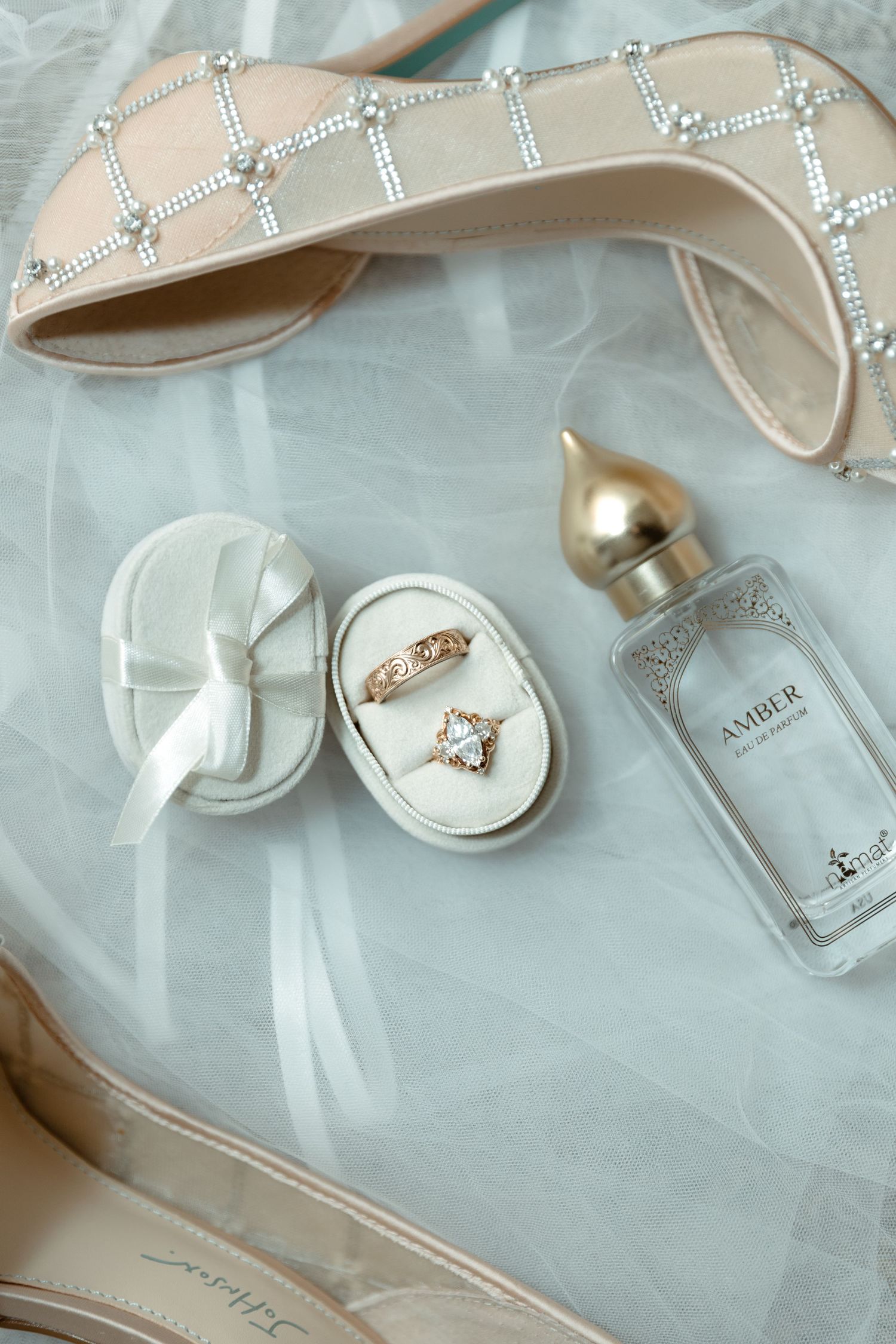 Wedding flat lay featuring diamond heels, gold rings in a velvet box, and amber perfume.