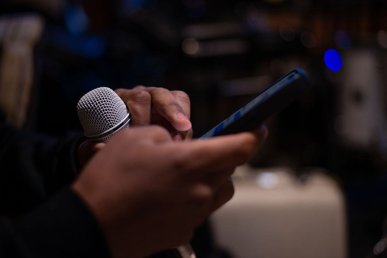Close-up of hands holding a microphone and mobile phone in a dimly lit venue.