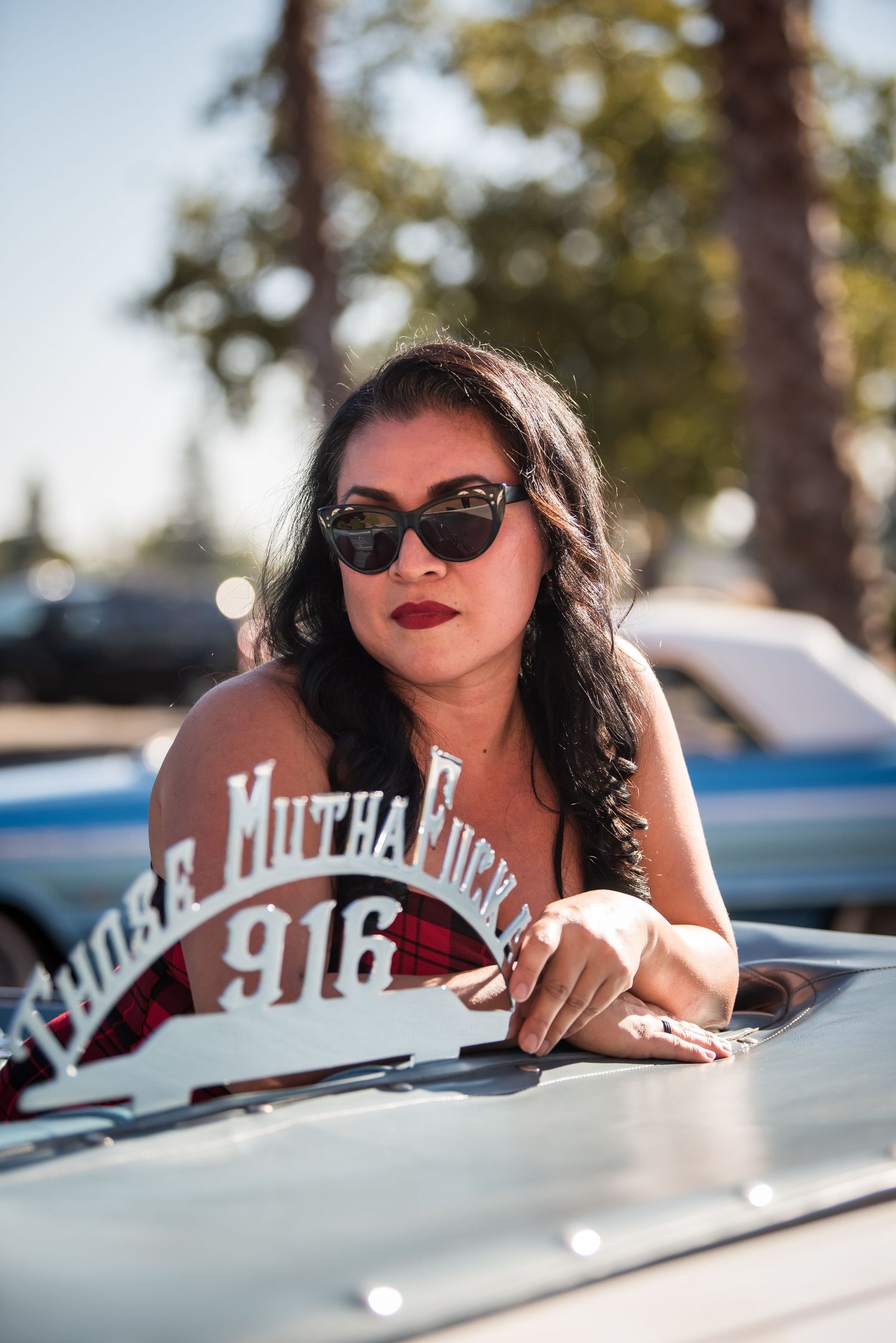 Lifestyle portrait of a woman in sunglasses posing with a classic car in golden sunlight.