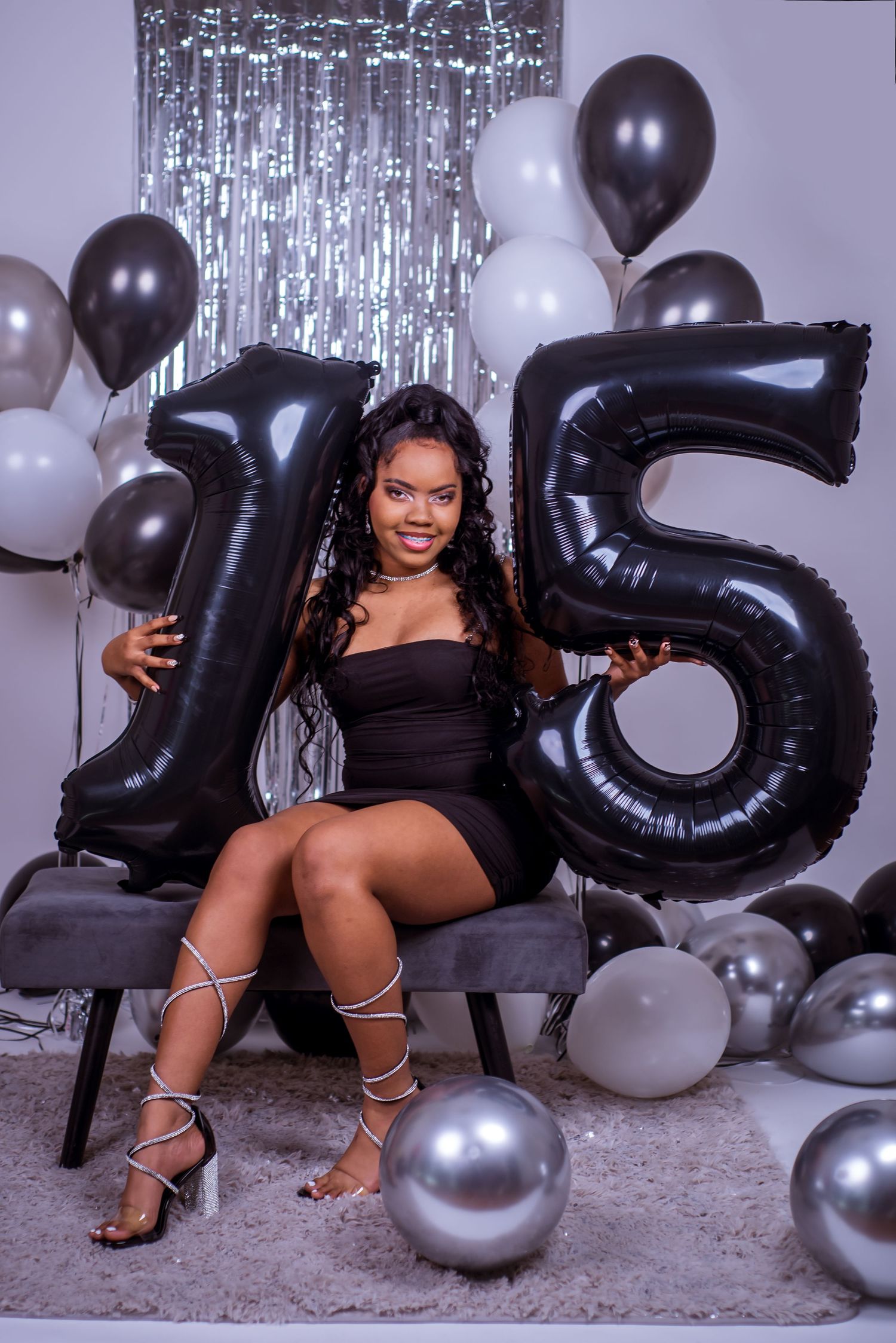 Silver and black balloons create a festive party atmosphere with sparkly tinsel backdrop and elegant decorations.