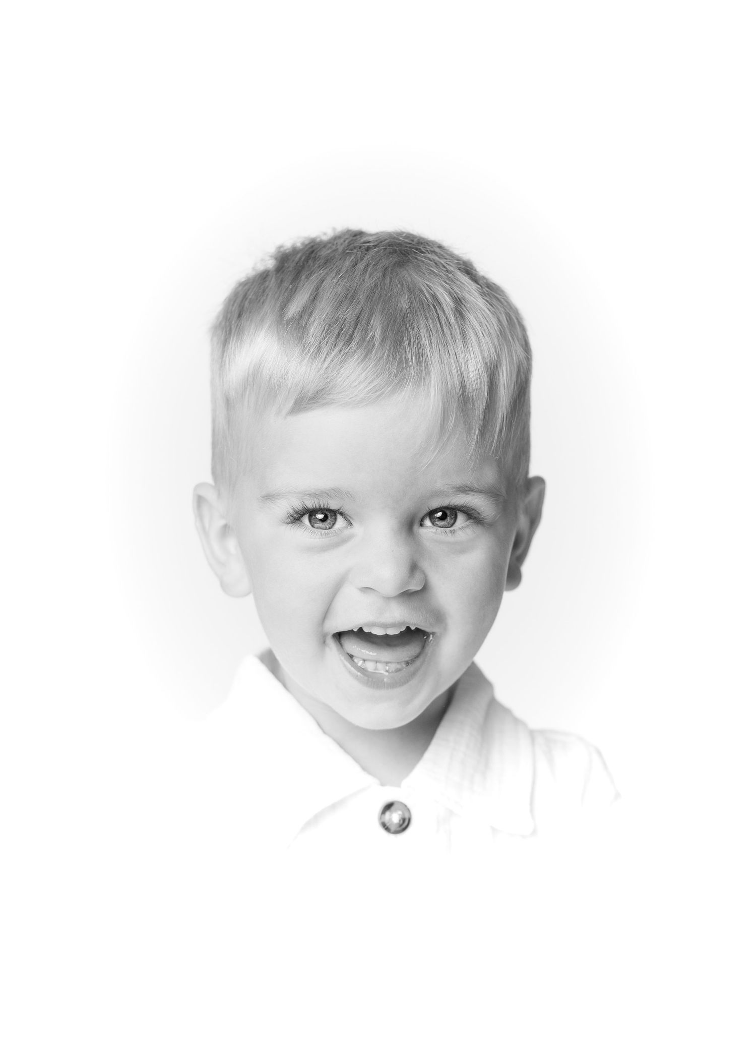 Black and white portrait of a smiling young blonde boy wearing a white collared shirt.