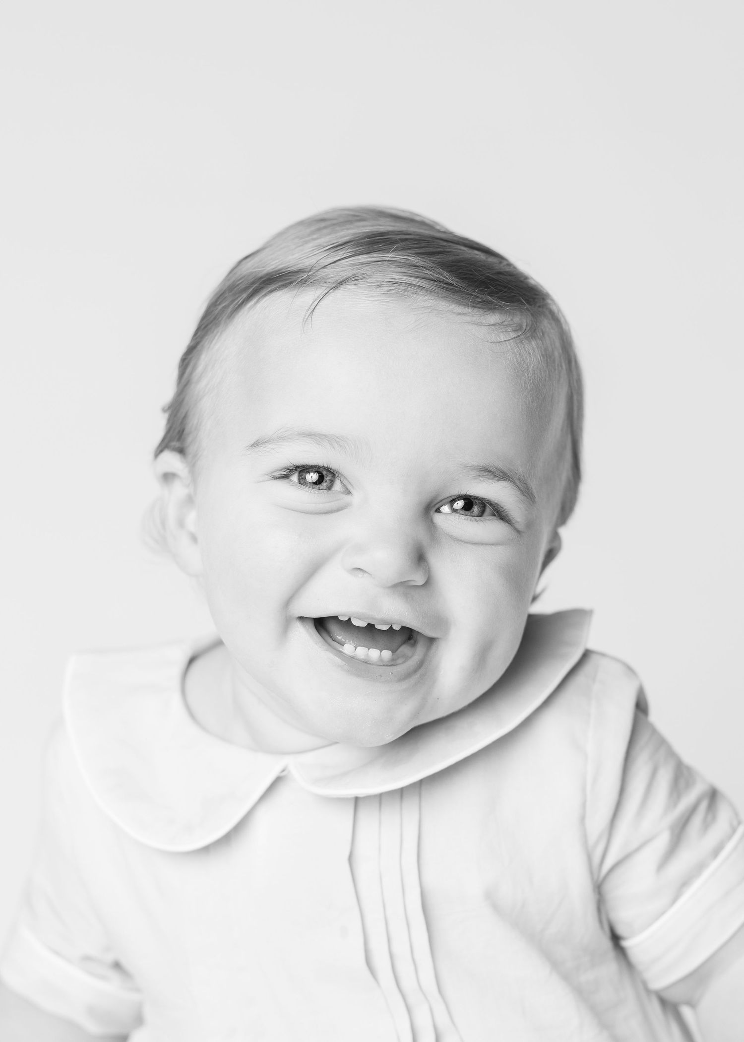 Black and white portrait of a smiling baby wearing a white Peter Pan collar outfit.