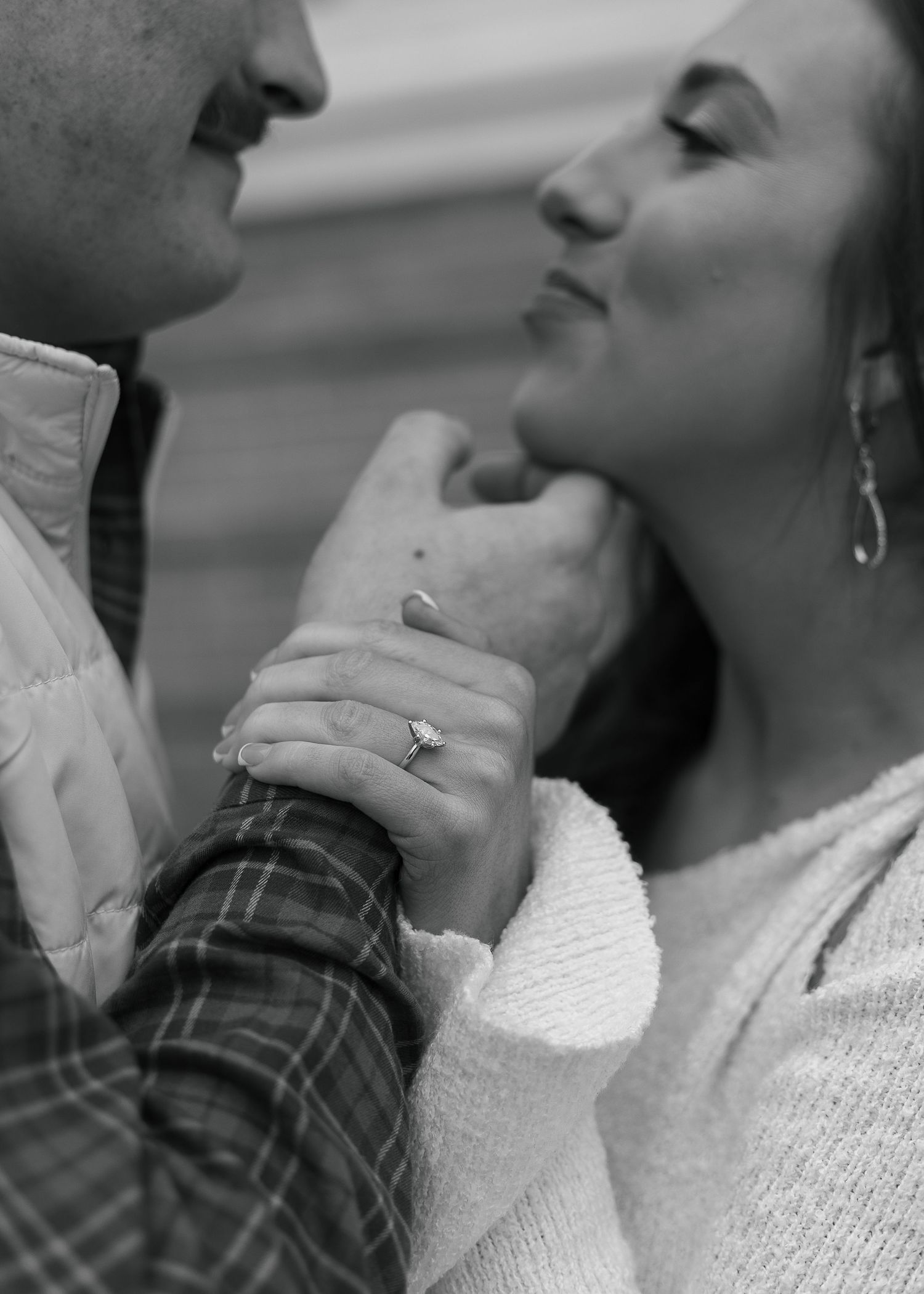 Black and white photo of a couple holding hands, showcasing an engagement ring, in a tender romantic moment.