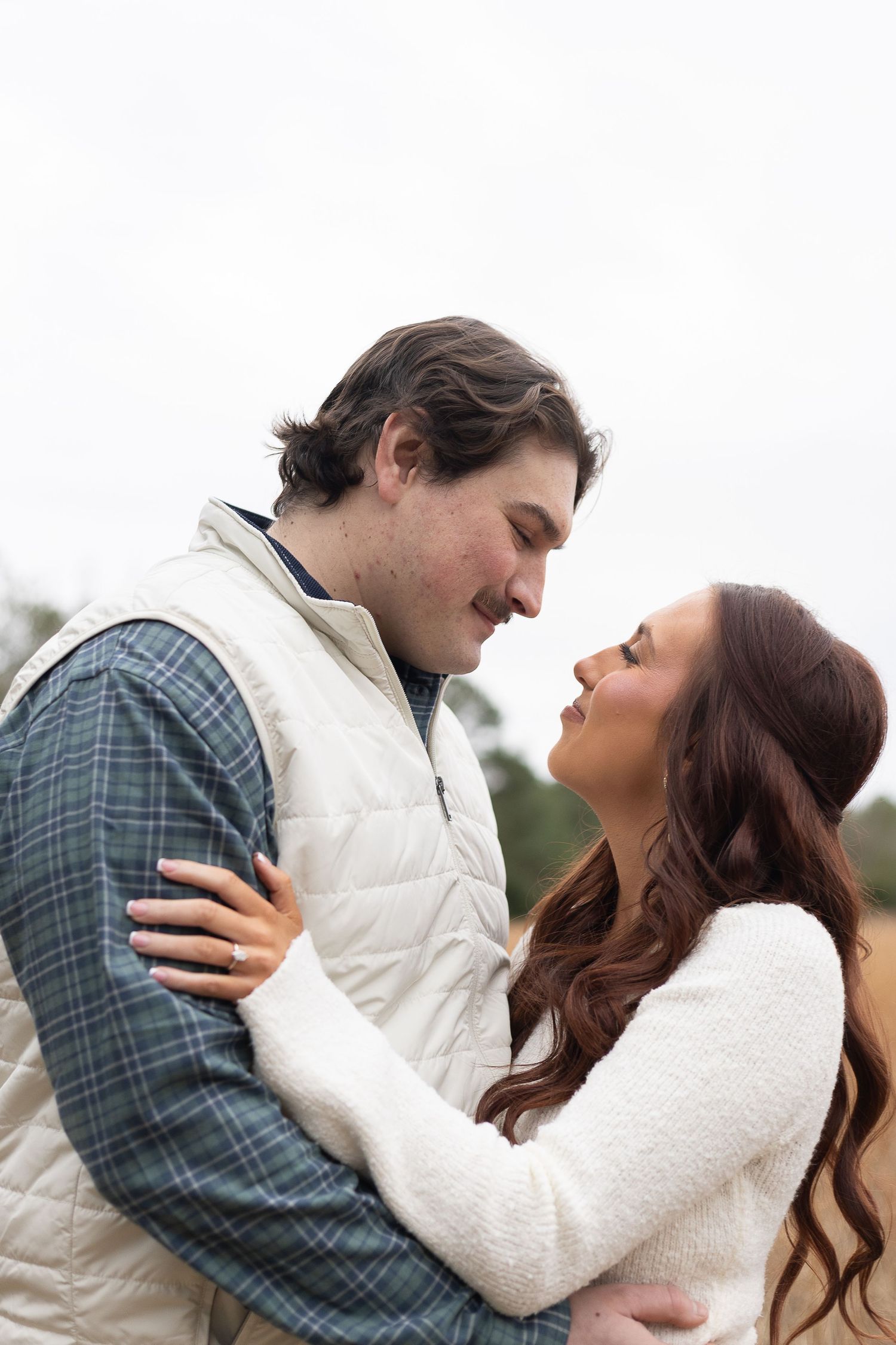 Couple sharing a romantic moment outdoors, man in plaid shirt and vest, woman in white sweater, nearly kissing.