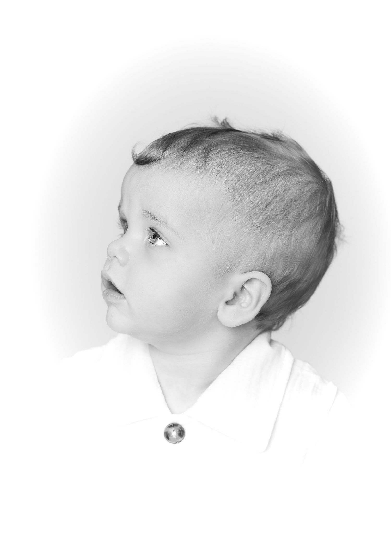 Black and white portrait of a curious toddler boy looking up, wearing a white shirt with a small button.